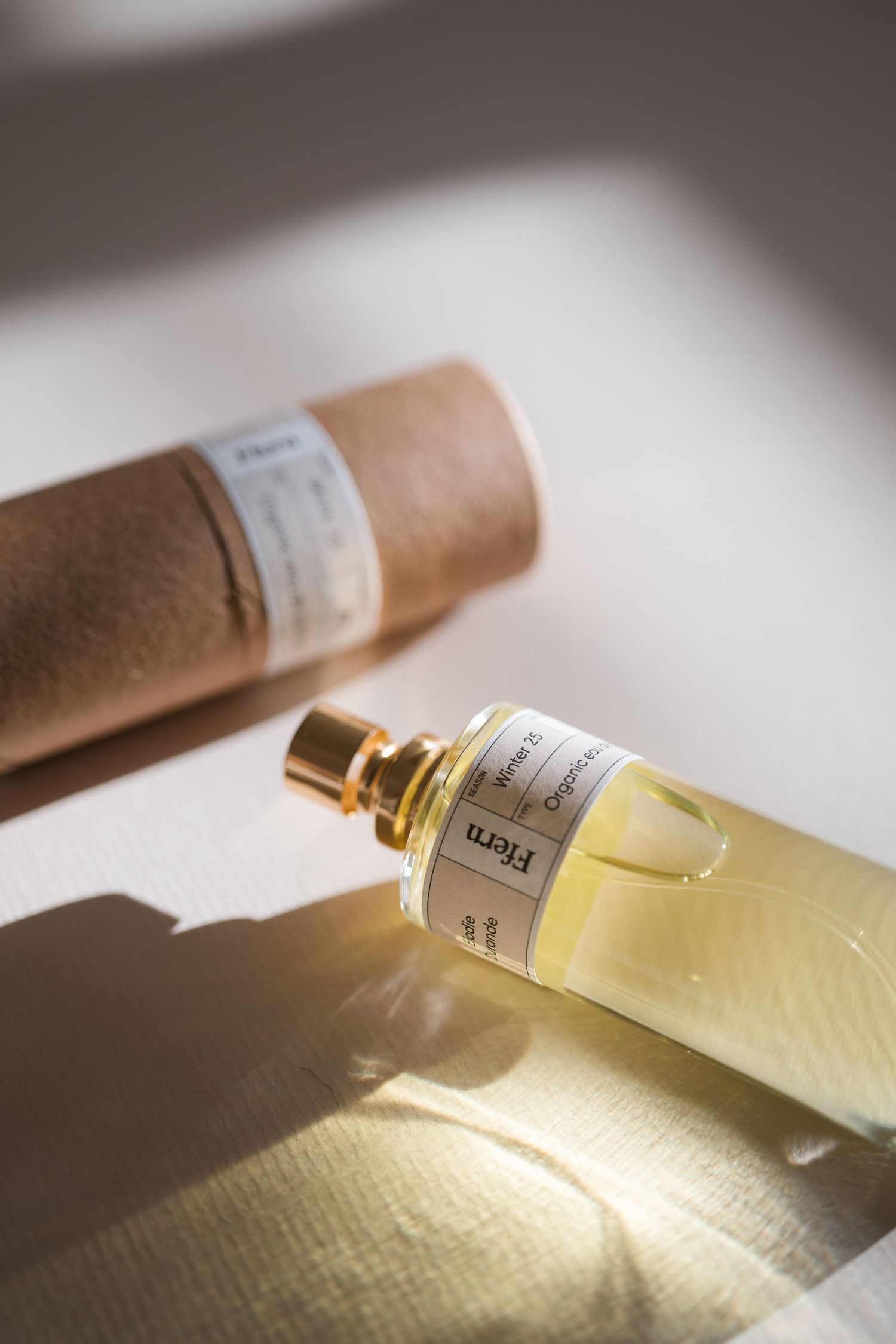A glass bottle of yellow perfume laying on its side casting a soft shadow in natural light.