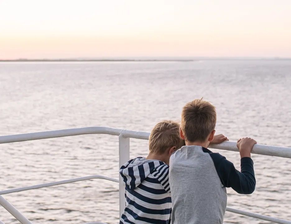 Two children sitting together on a railing, watching the sea at sunset.