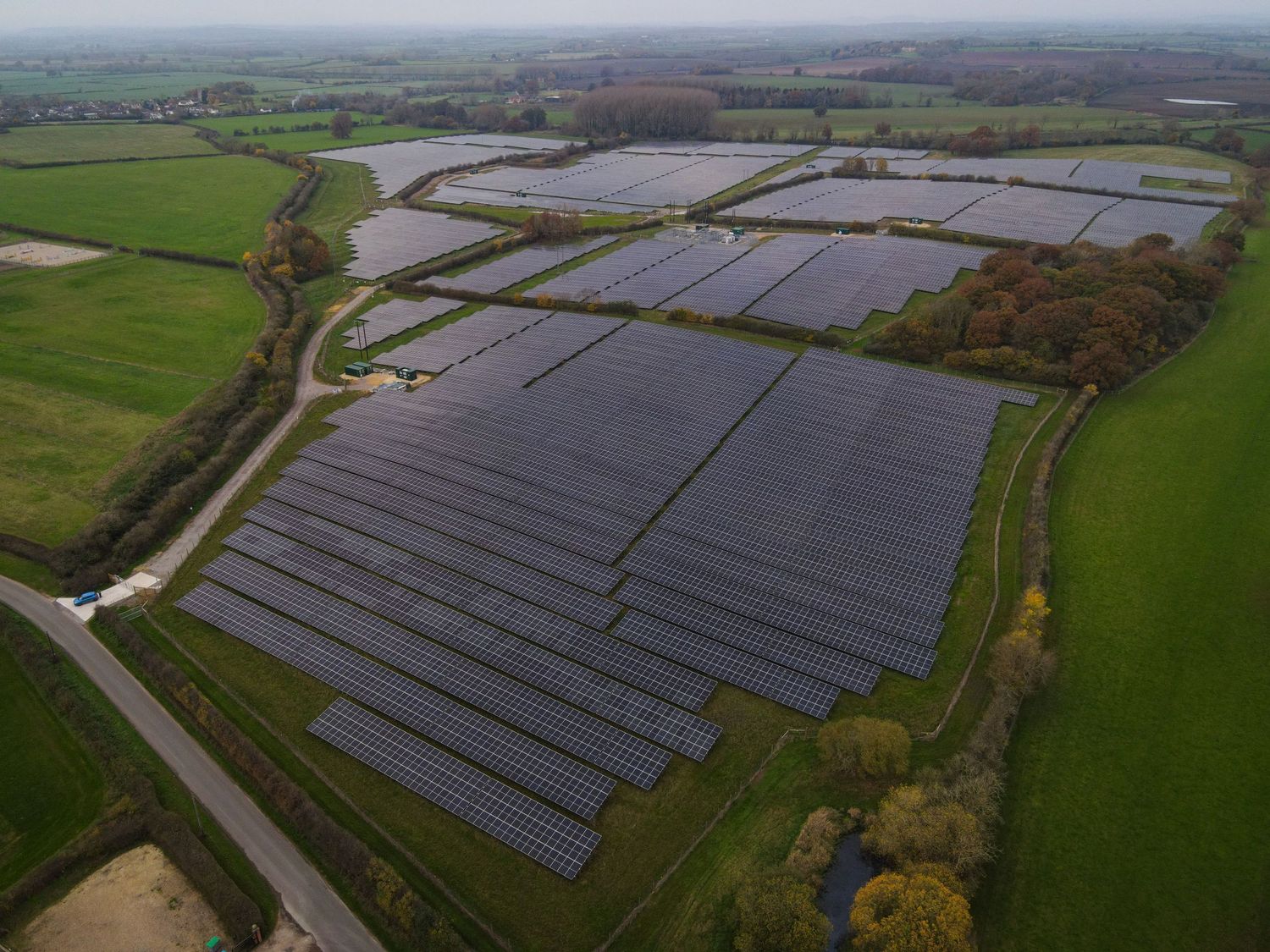 Aerial view of large solar panel farm installation in rural countryside with green fields surrounding the installation.