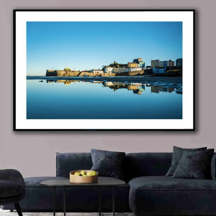 Waterfront houses and buildings perfectly reflected in calm waters against blue sky, displayed in modern living room frame.