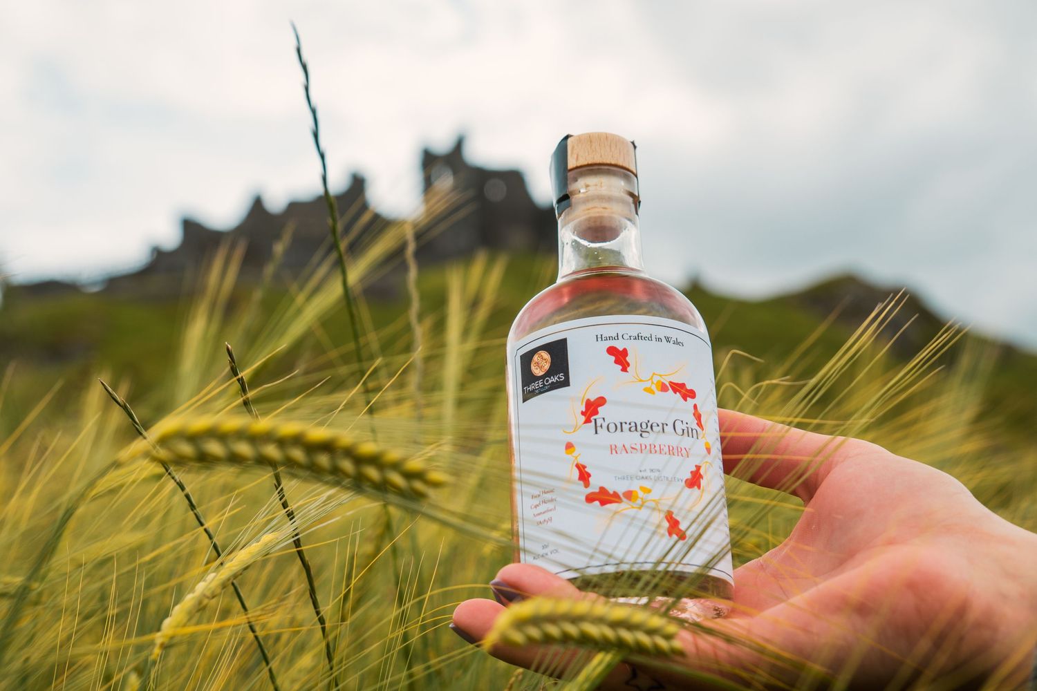 A bottle of vodka held up against a backdrop of golden wheat stalks and cloudy sky.