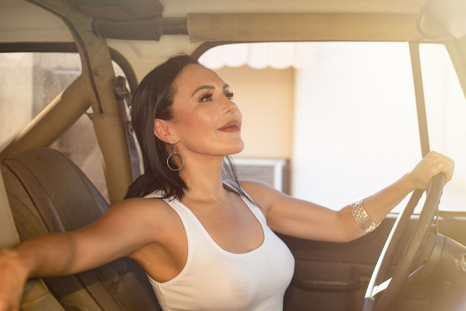 Woman smiling while driving car on sunny day.