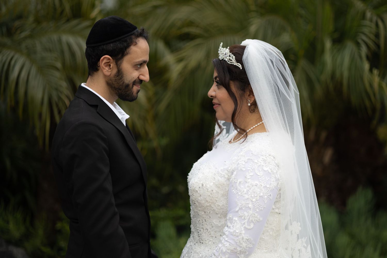 A couple shares an intimate moment during their outdoor wedding ceremony against a backdrop of lush tropical palms.