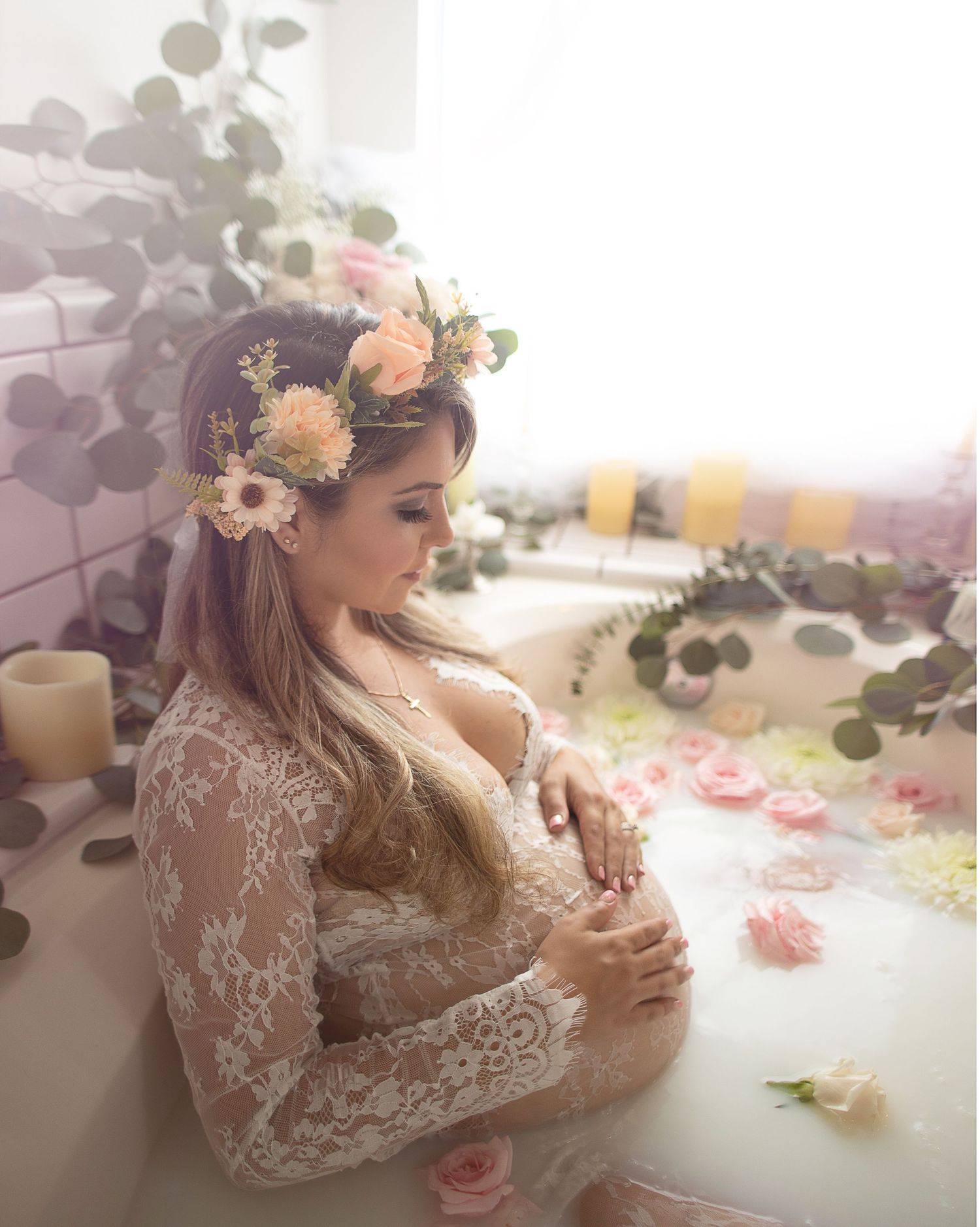 A maternity photo with lace dress and floral crown in soft dreamy lighting with scattered rose petals.