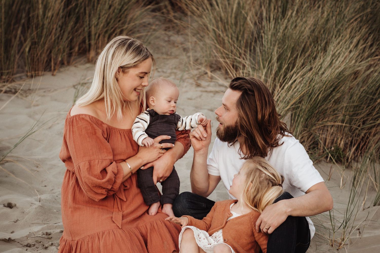 Family bonding moment on a sandy beach with tall grass in the background.