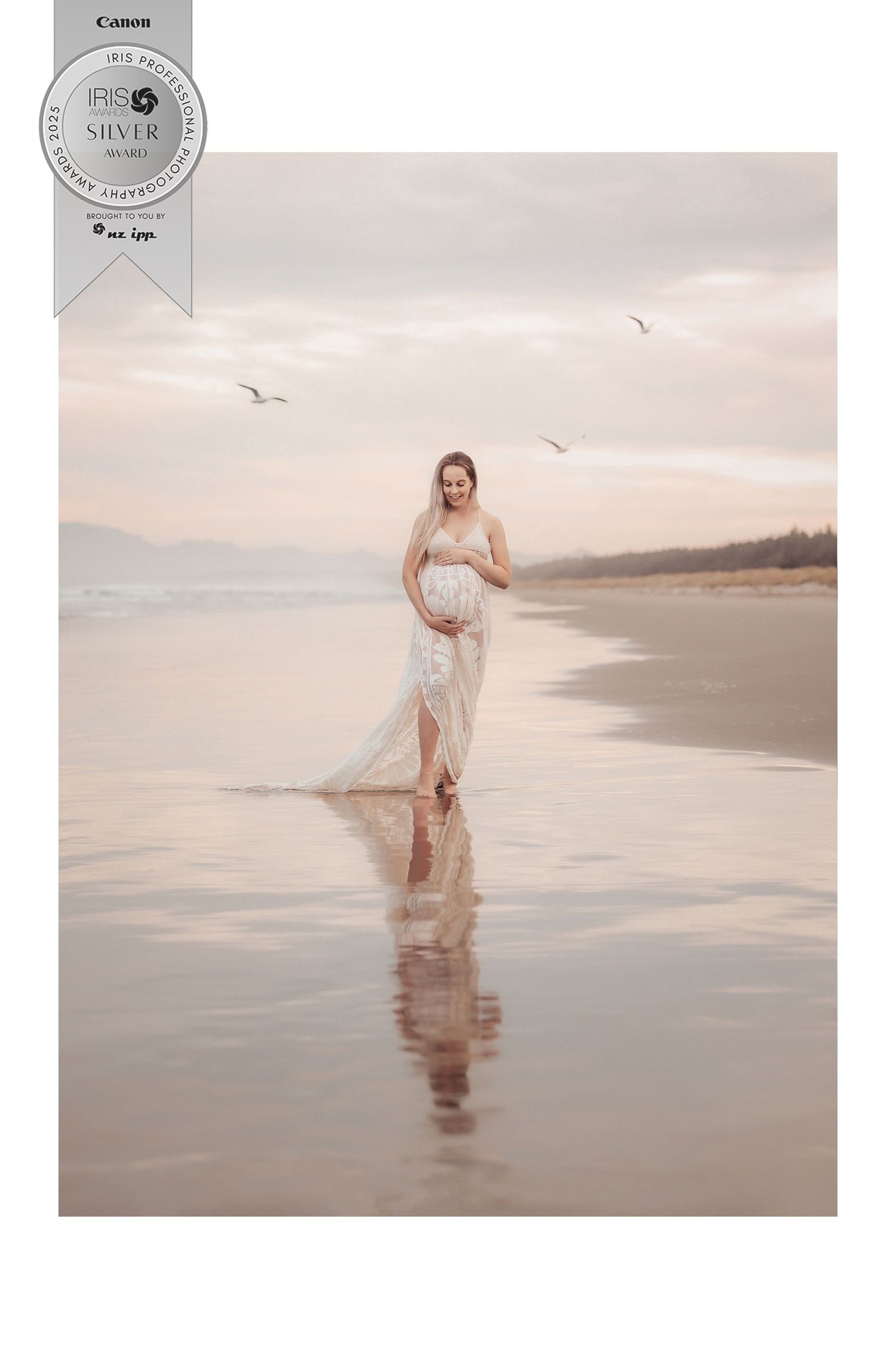 A dreamy beach maternity photoshoot at sunset with soft reflections on wet sand and seagulls flying overhead.