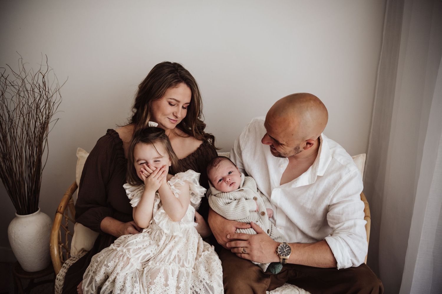 A loving family shares tender moments together while relaxing on a couch in elegant neutral-colored attire.