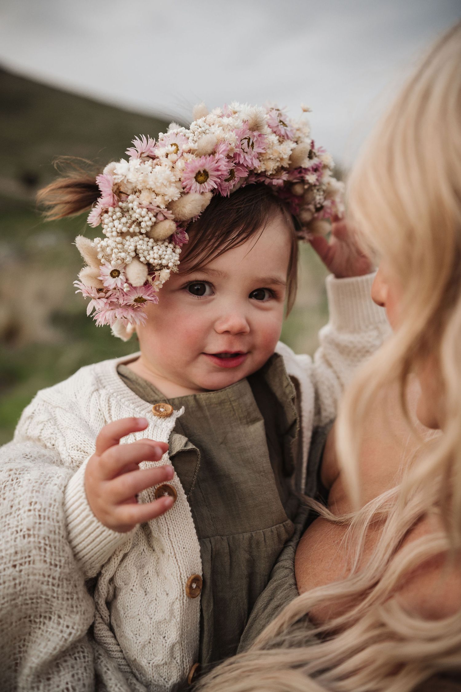 Young child wearing floral crown and knit sweater smiles sweetly.