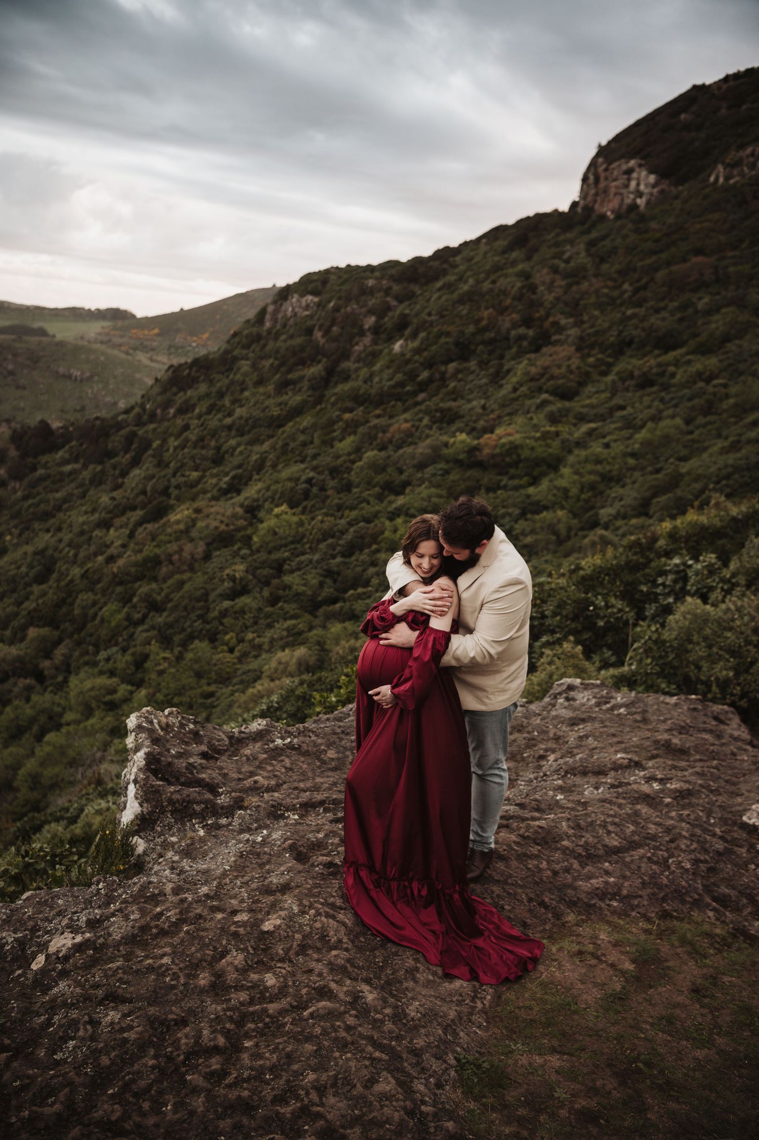 Romantic maternity moment on a rocky cliff overlooking mountain vistas.