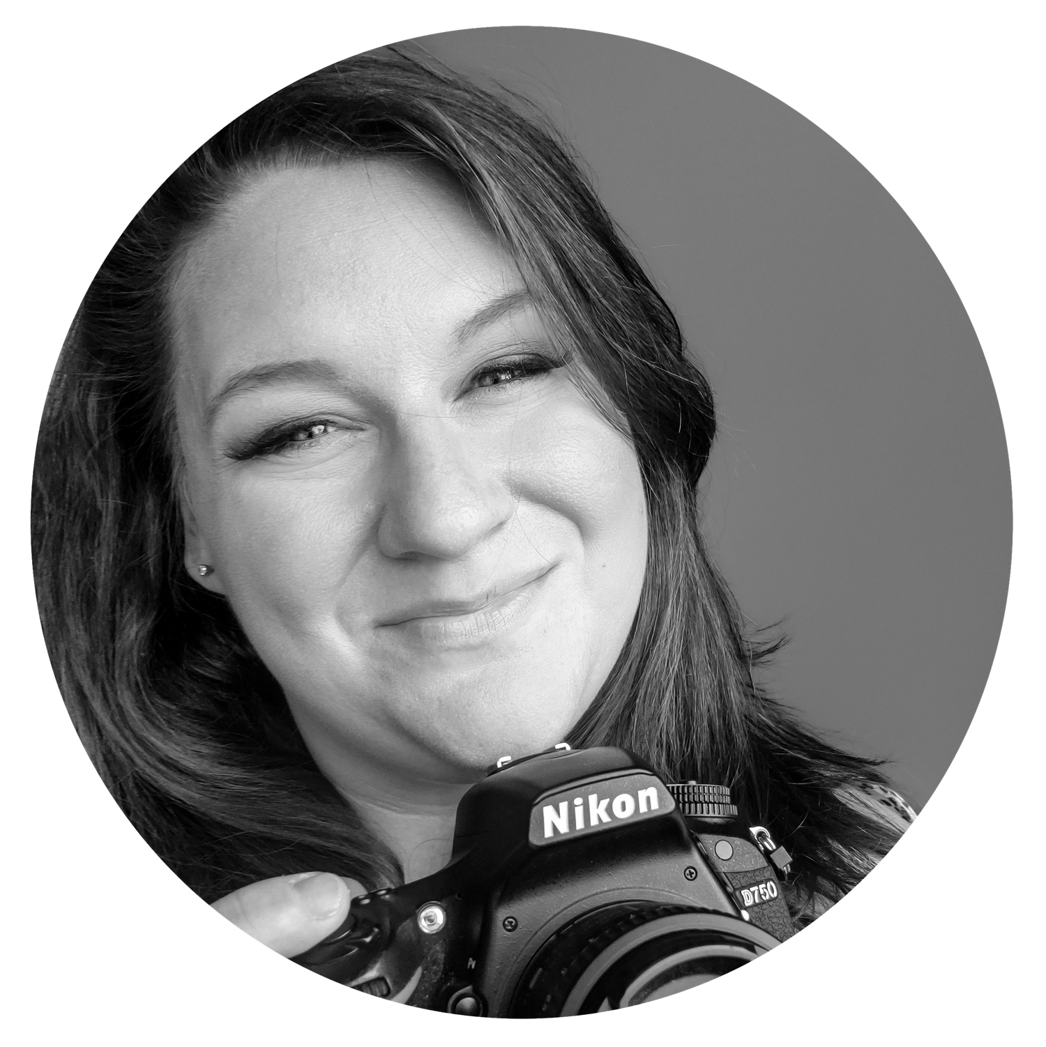 Professional photographer smiling while holding a Nikon camera against grey background.