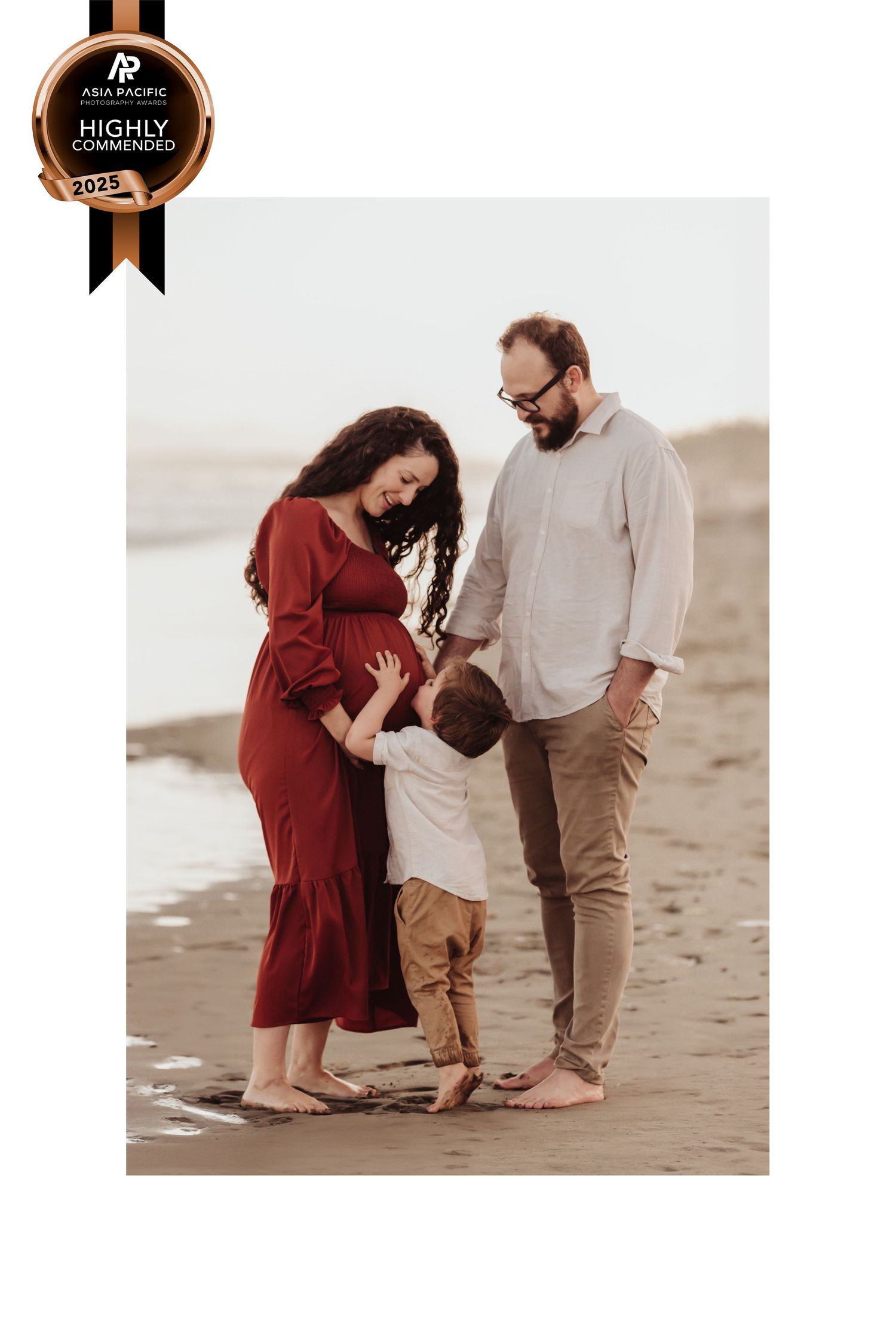 Family wearing beige and red outfits walks together barefoot along a beach at sunset.