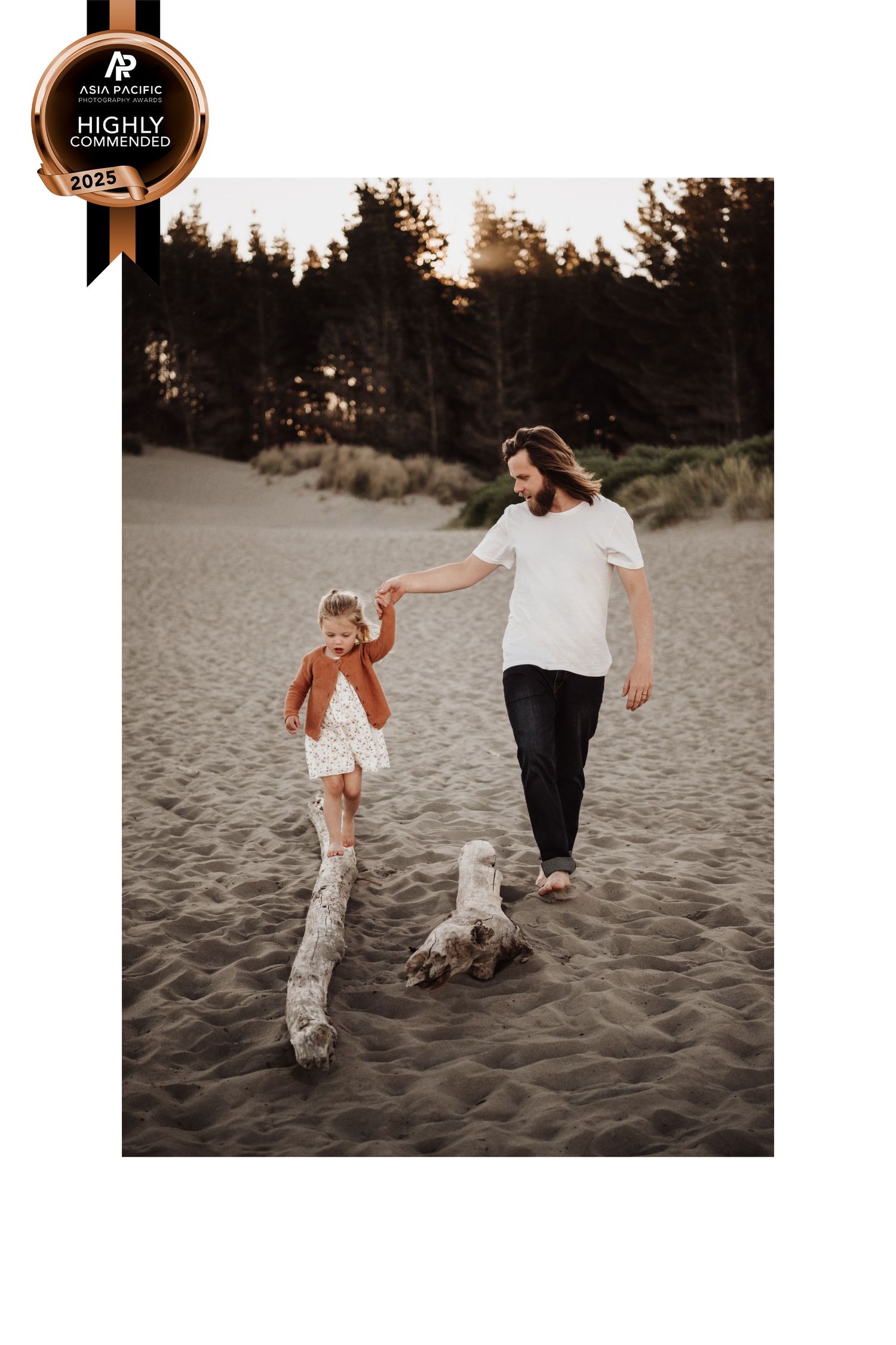 Two people walking together on a sandy beach at sunset with pine trees in the background.
