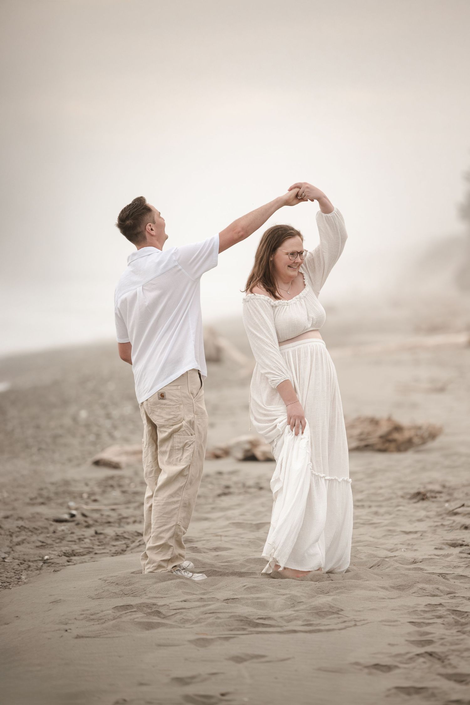 Two people in white outfits dance together gracefully on a misty beach at sunset.
