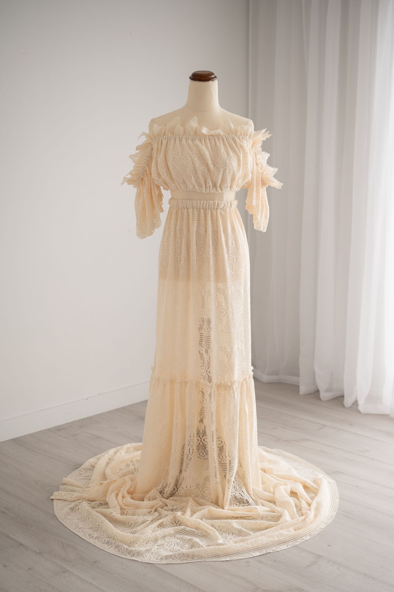 Vintage off-shoulder ivory lace wedding dress with ruffled sleeves and long flowing train displayed on mannequin.