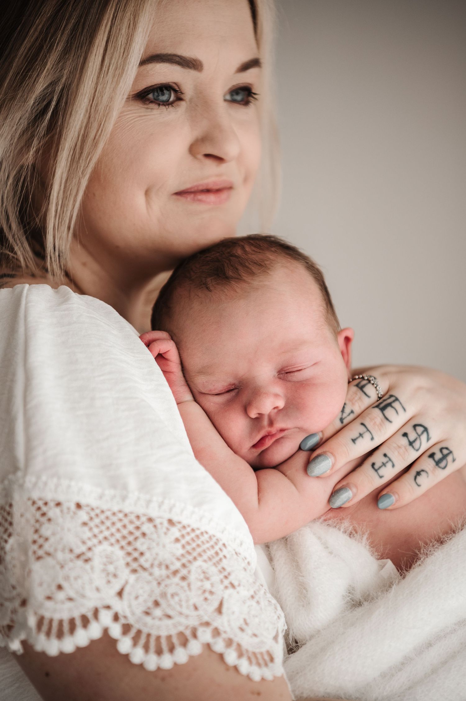 A tender moment captured as a sleeping newborn baby rests against a white lace sleeve while being cradled.