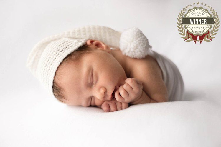 Sleeping newborn wearing knit hat with pom pom on white background.
