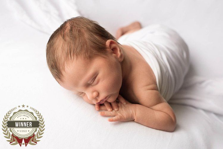 Peaceful sleeping newborn baby in white wrap lying on soft white backdrop.