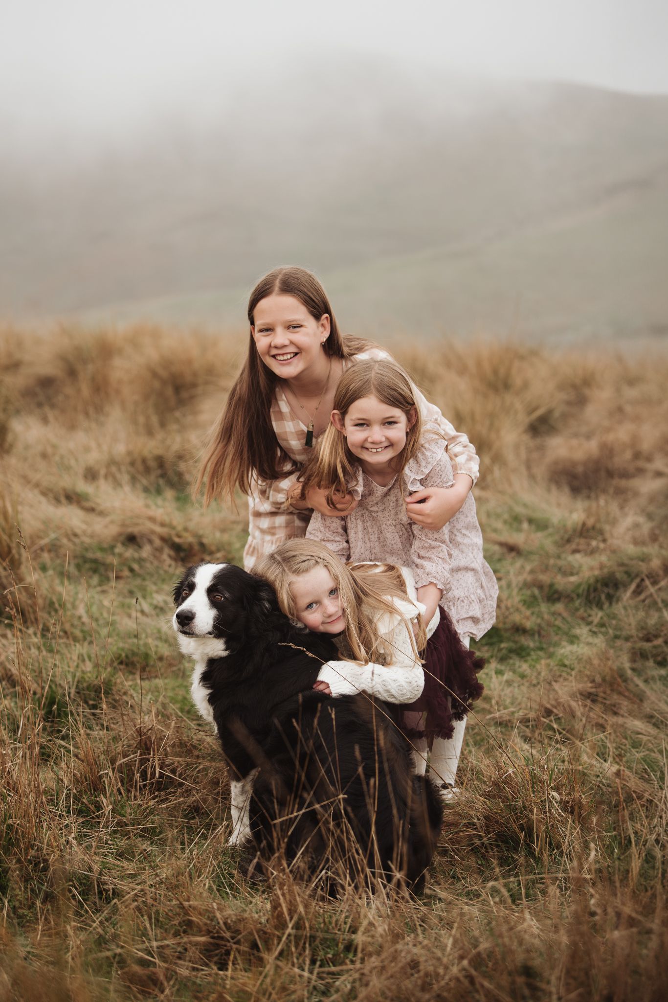 A playful family moment with children and a black and white dog in a misty field.