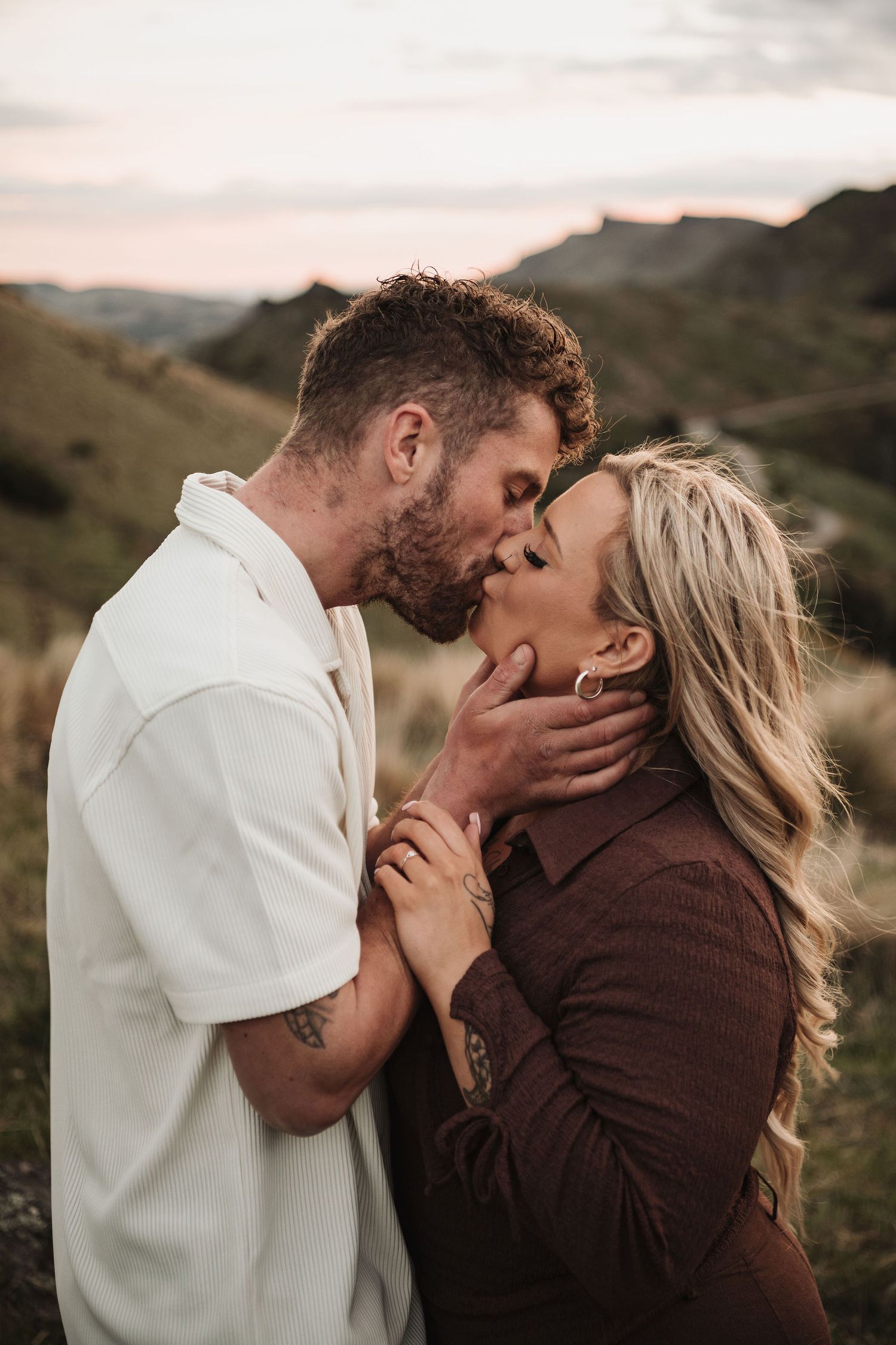 Romantic couple sharing an intimate kiss against a mountainous backdrop at sunset.