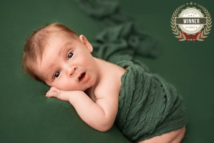 Alert baby lying on green blanket making expressive face during portrait session.
