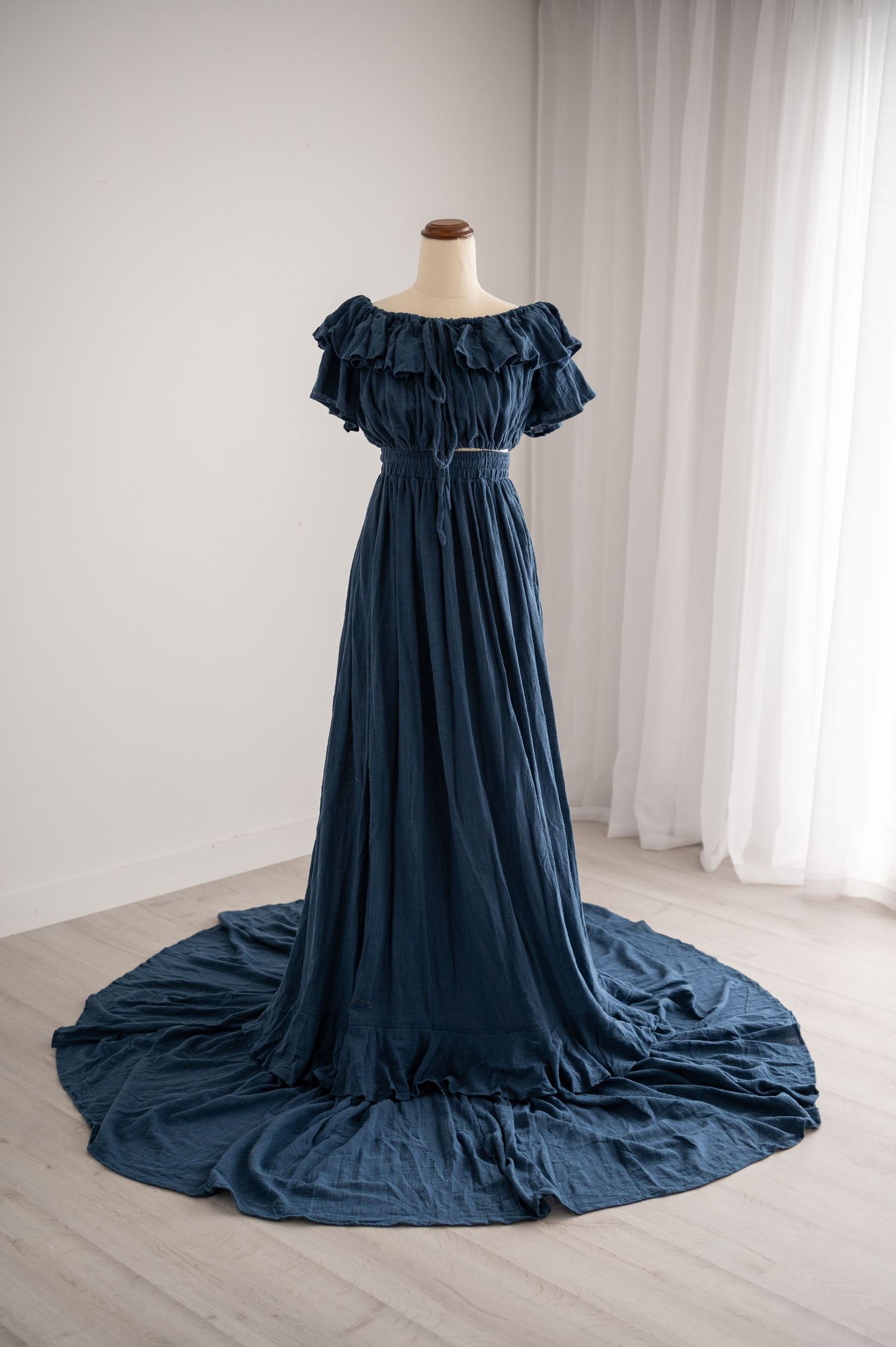 Navy blue maternity gown with off-shoulder neckline and flowing long train displayed on mannequin against white backdrop.