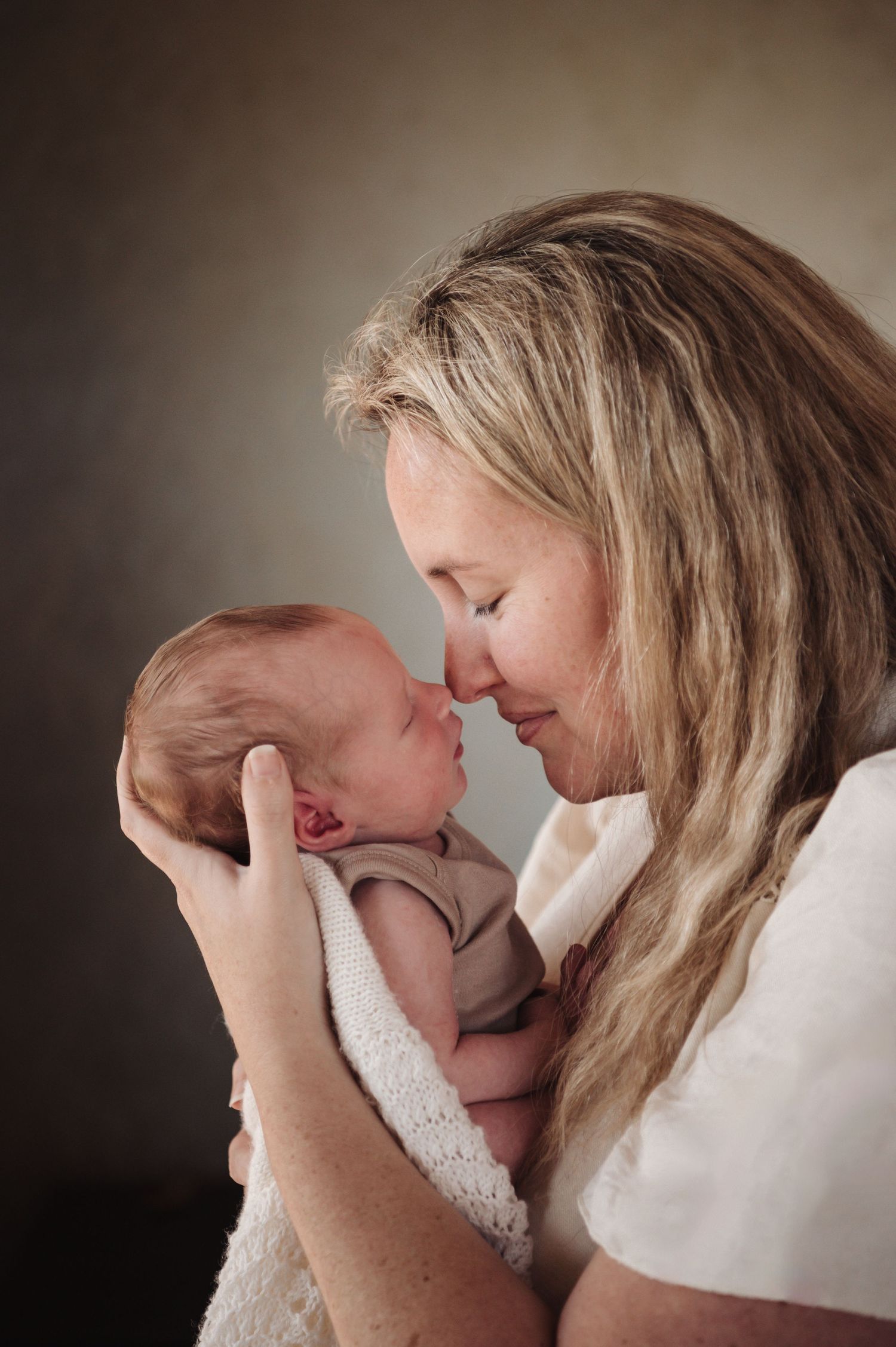 Tender moment between parent and newborn baby captured in soft lighting against dark background.