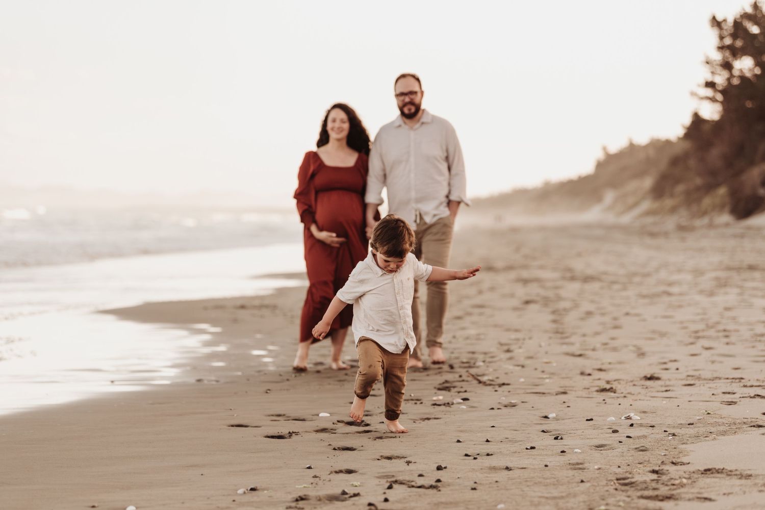 A family walks and plays together at sunset on a serene beach with footprints in the sand.