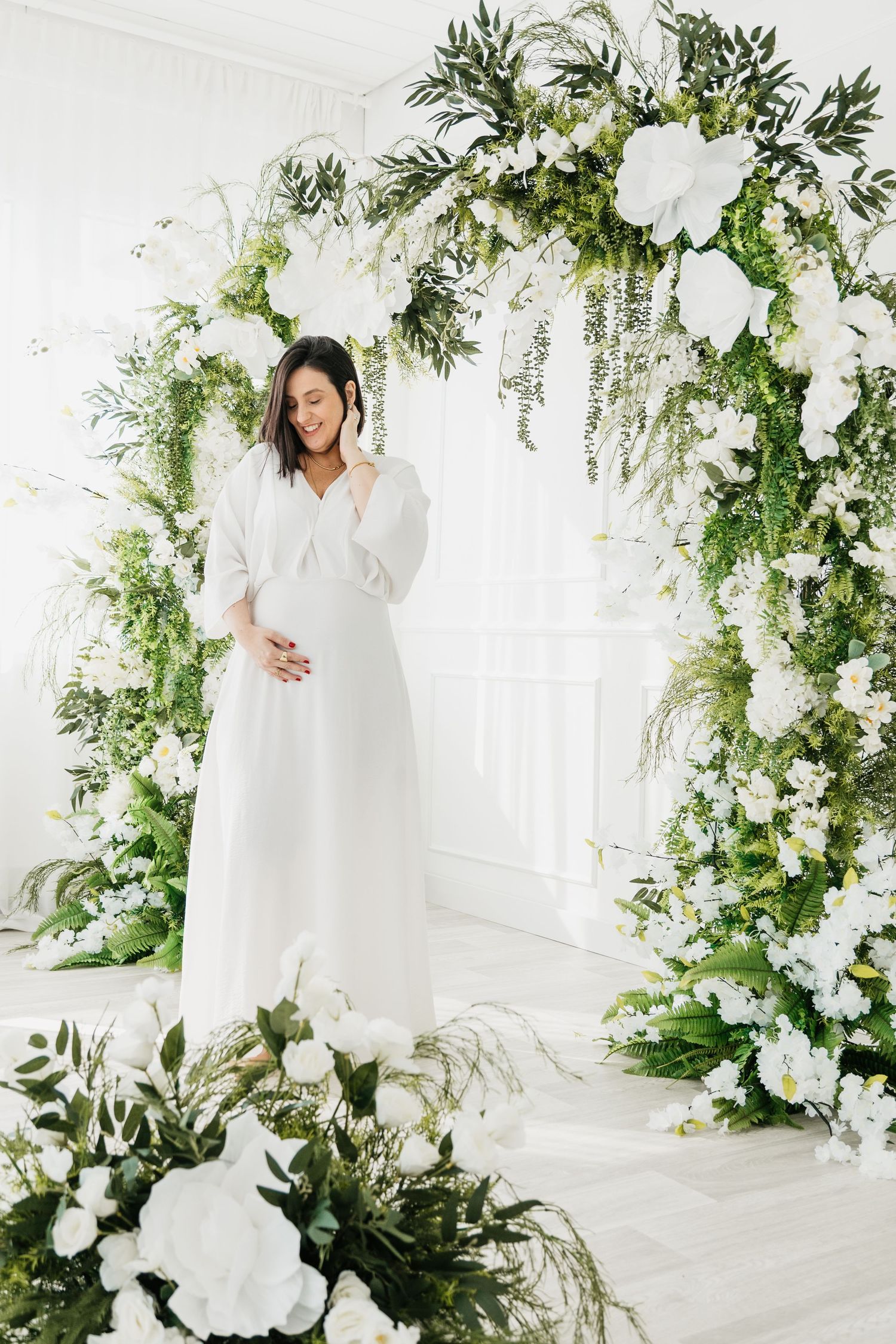 White floral wedding arch and decor with greenery against a bright white backdrop creates an elegant ceremony setting.