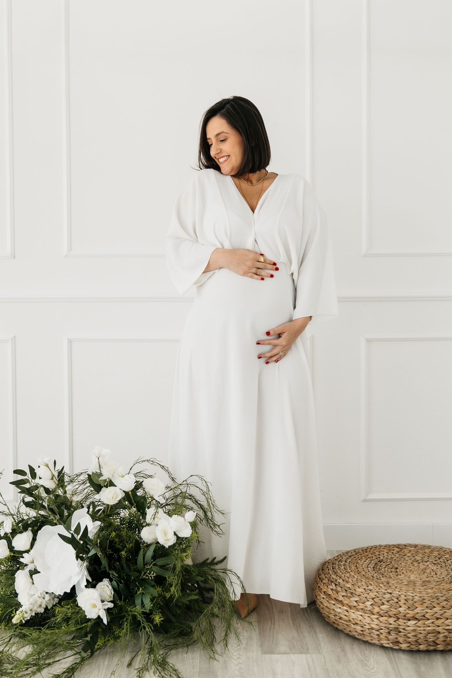 A series of minimalist maternity photos showing a white dress against light walls with natural wicker and floral accents.