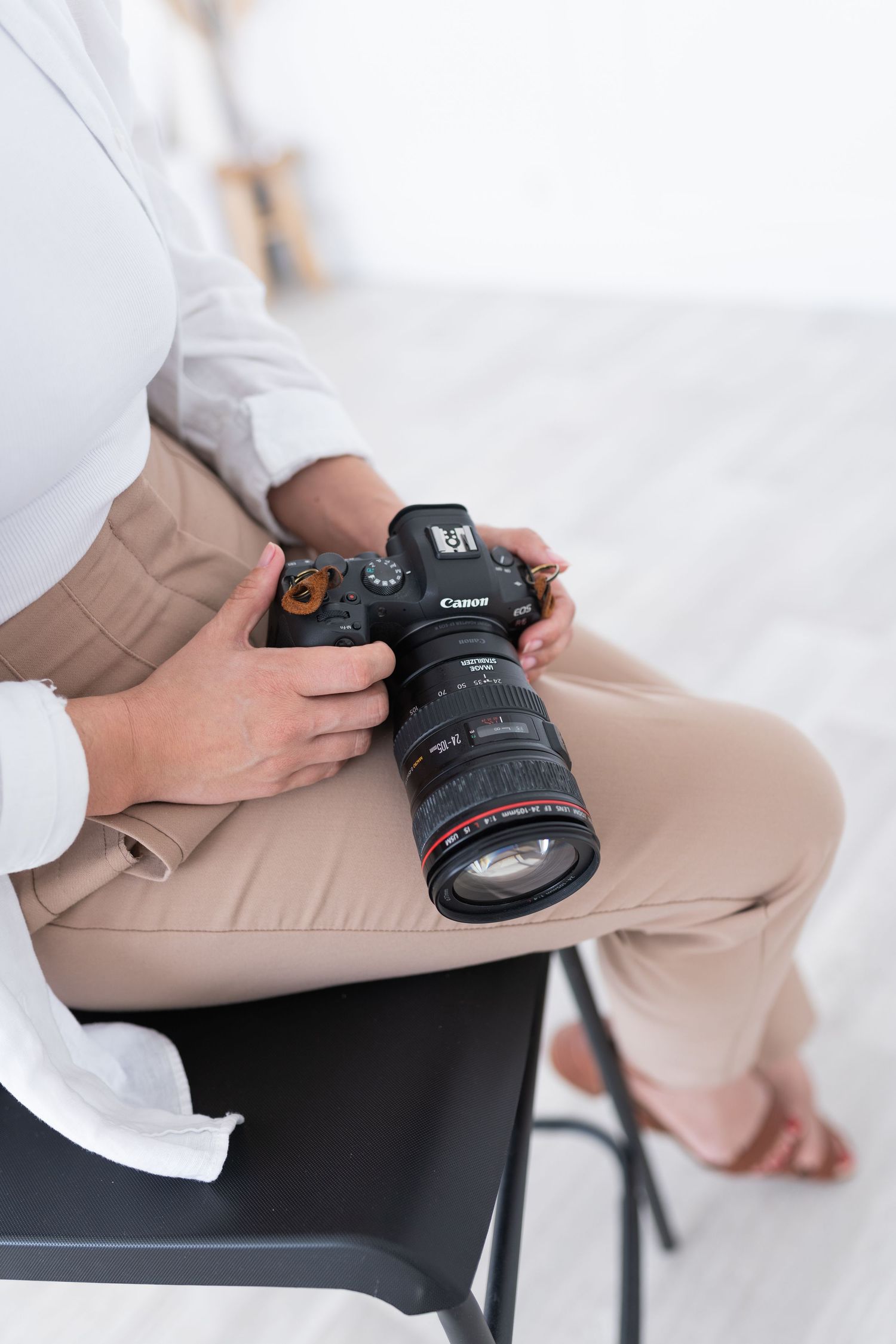 Professional photographer holding a Canon DSLR camera with telephoto lens while sitting in khaki pants and white shirt.