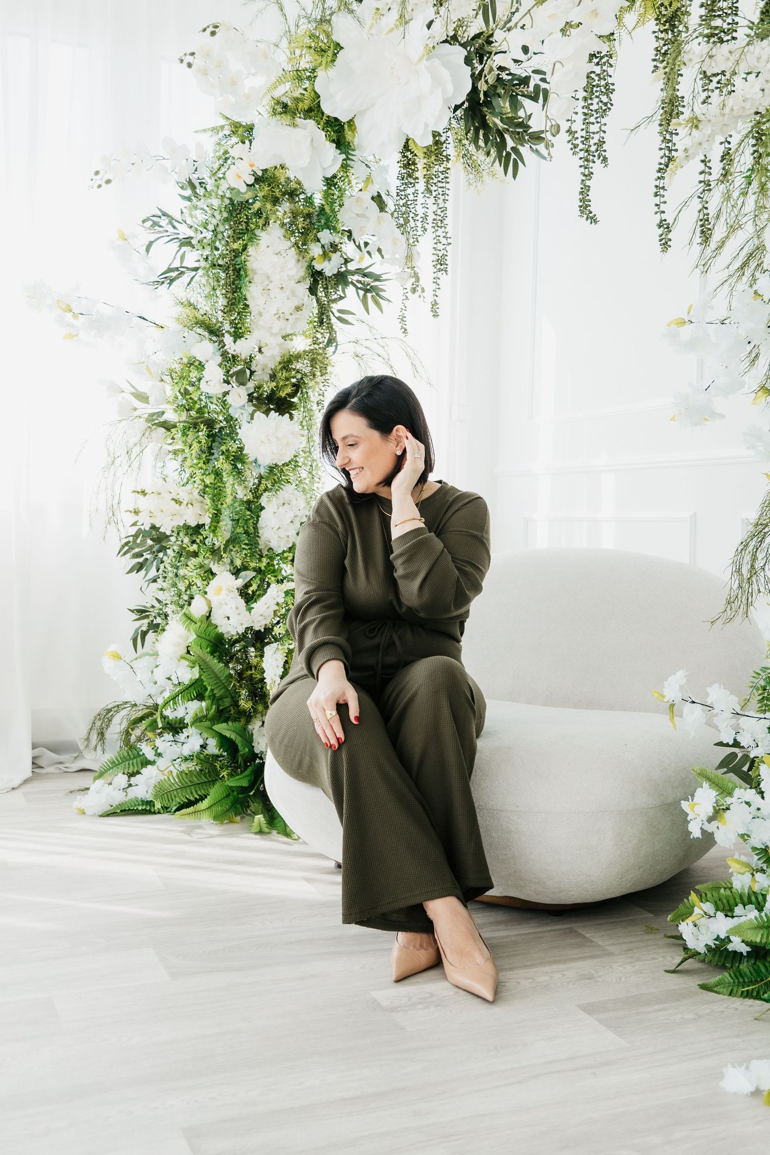 A figure sits in contemplative poses against a white backdrop adorned with cascading greenery and delicate white flowers.