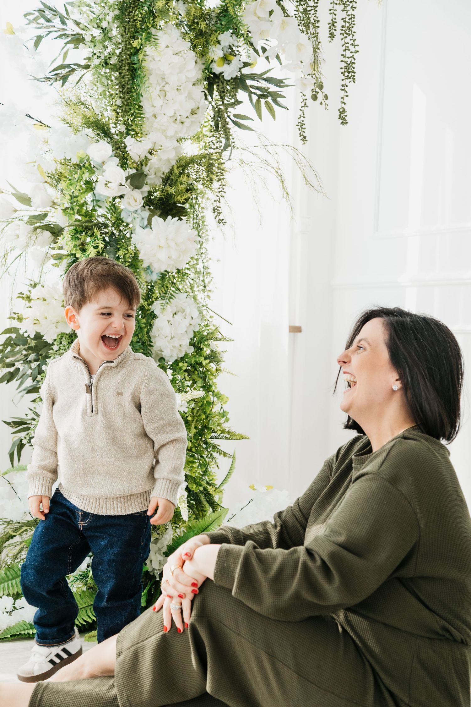 A joyful moment shared between a child in a cream sweater and woman in olive green against a floral backdrop.