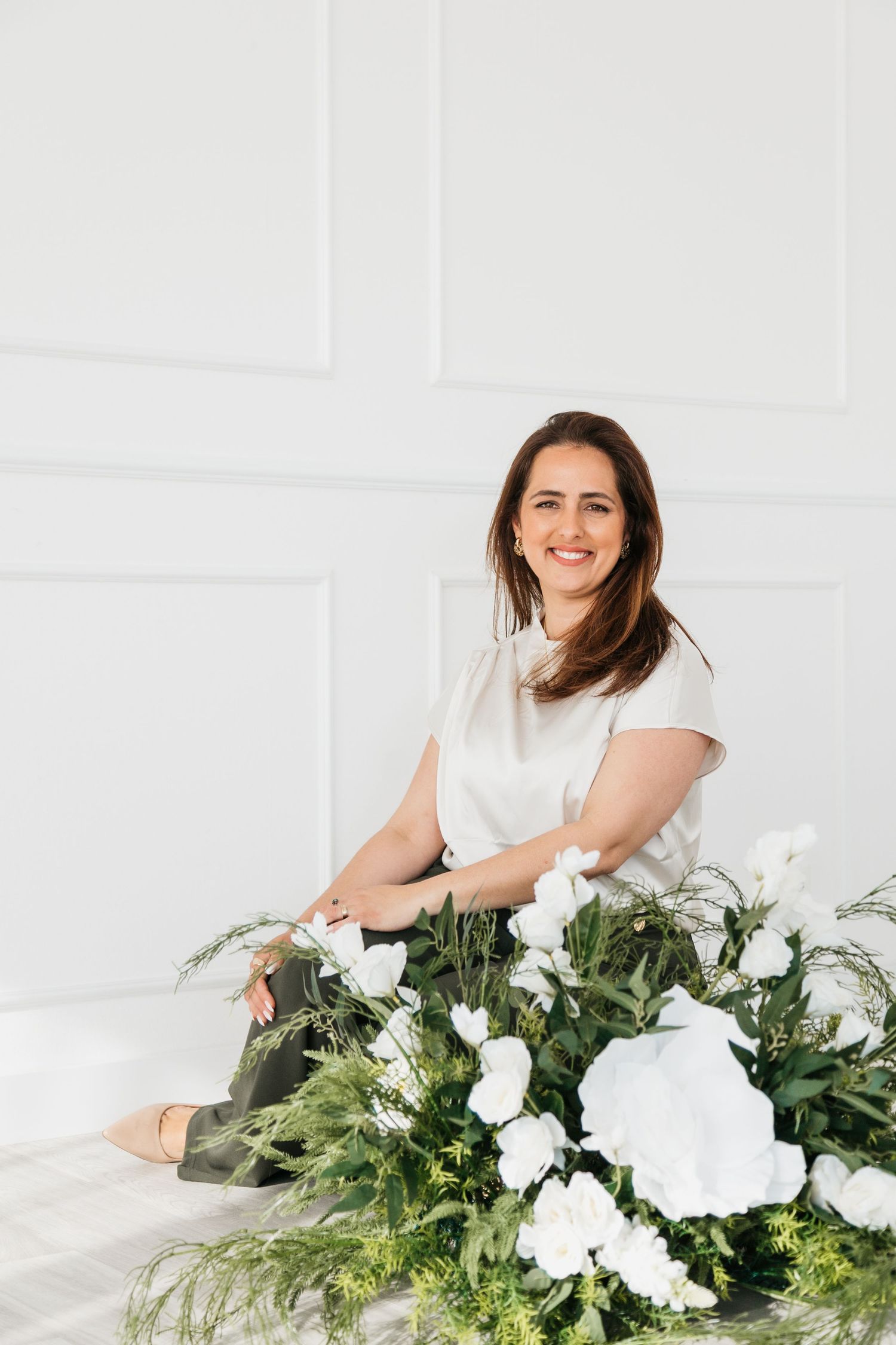 Florist arranges lush white flowers and greenery on white surface in bright studio setting.