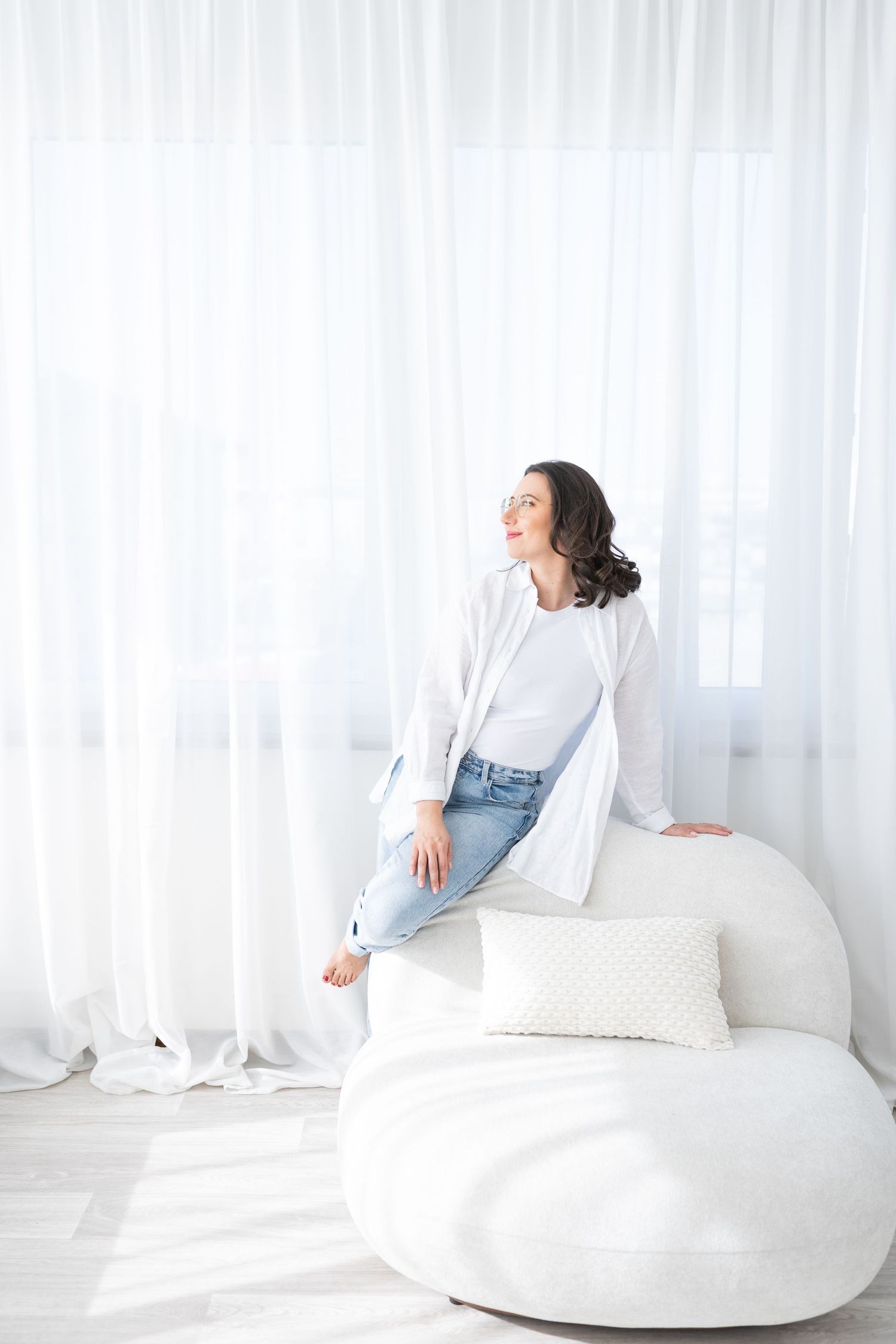 Person in white clothing lounges on plush white furniture against a bright white backdrop in a minimalist setting.