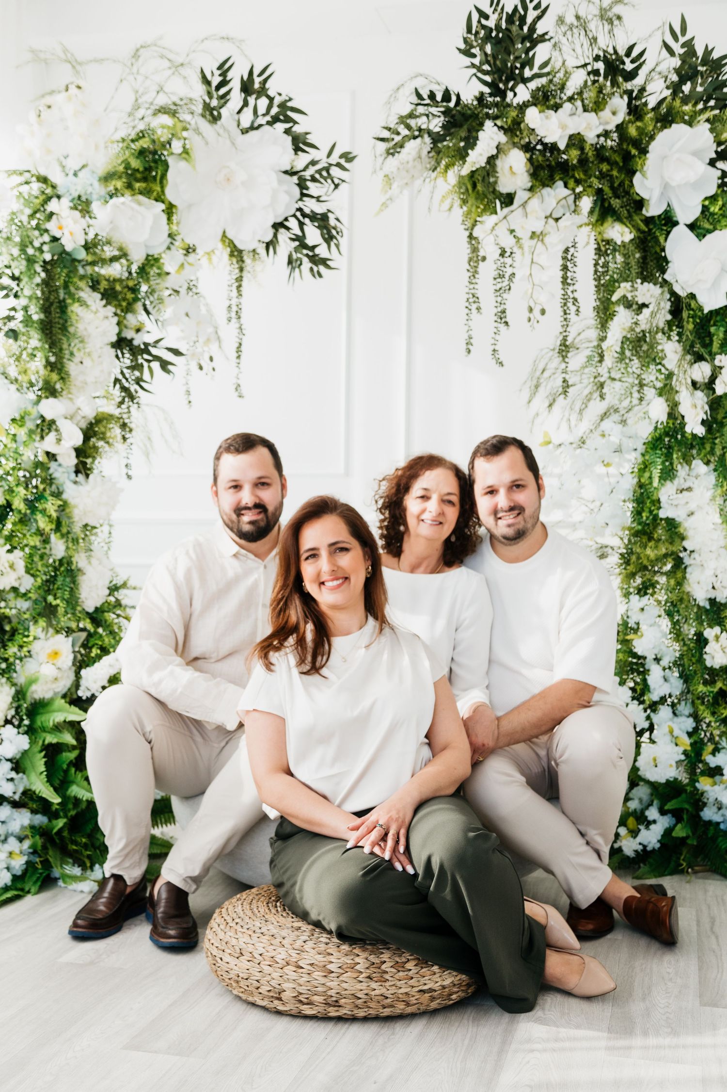 Family portrait session with matching white shirts against floral backdrop in studio setting.