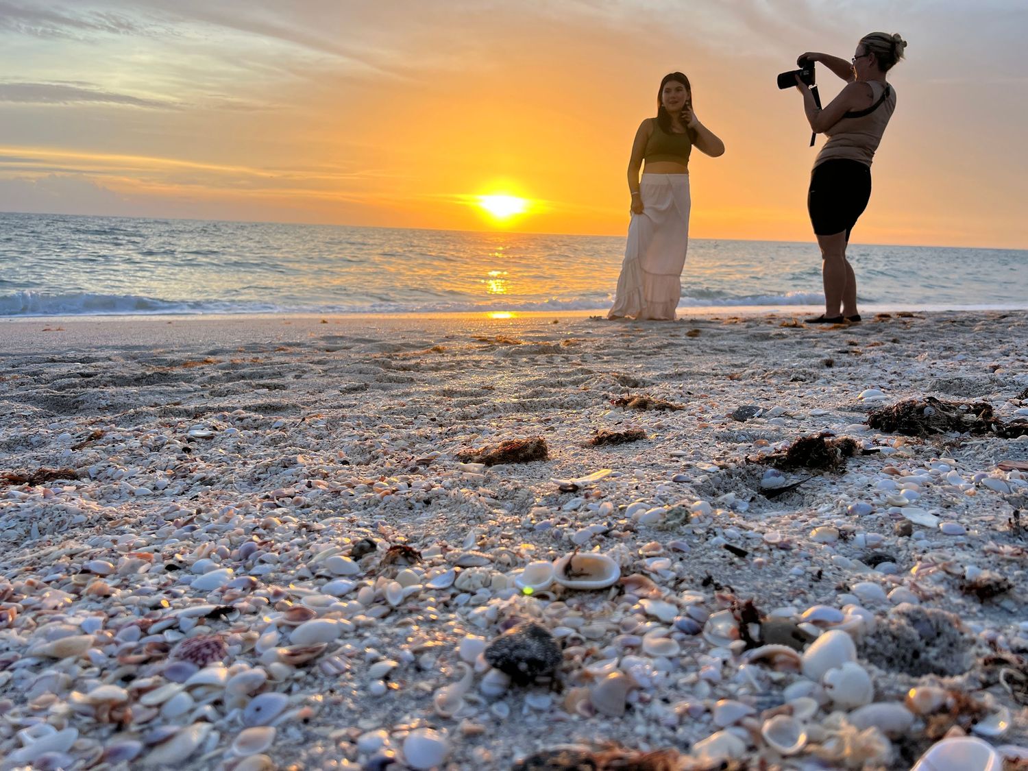Photographer capturing woman in yellow top and white skirt at stunning golden beach sunset.