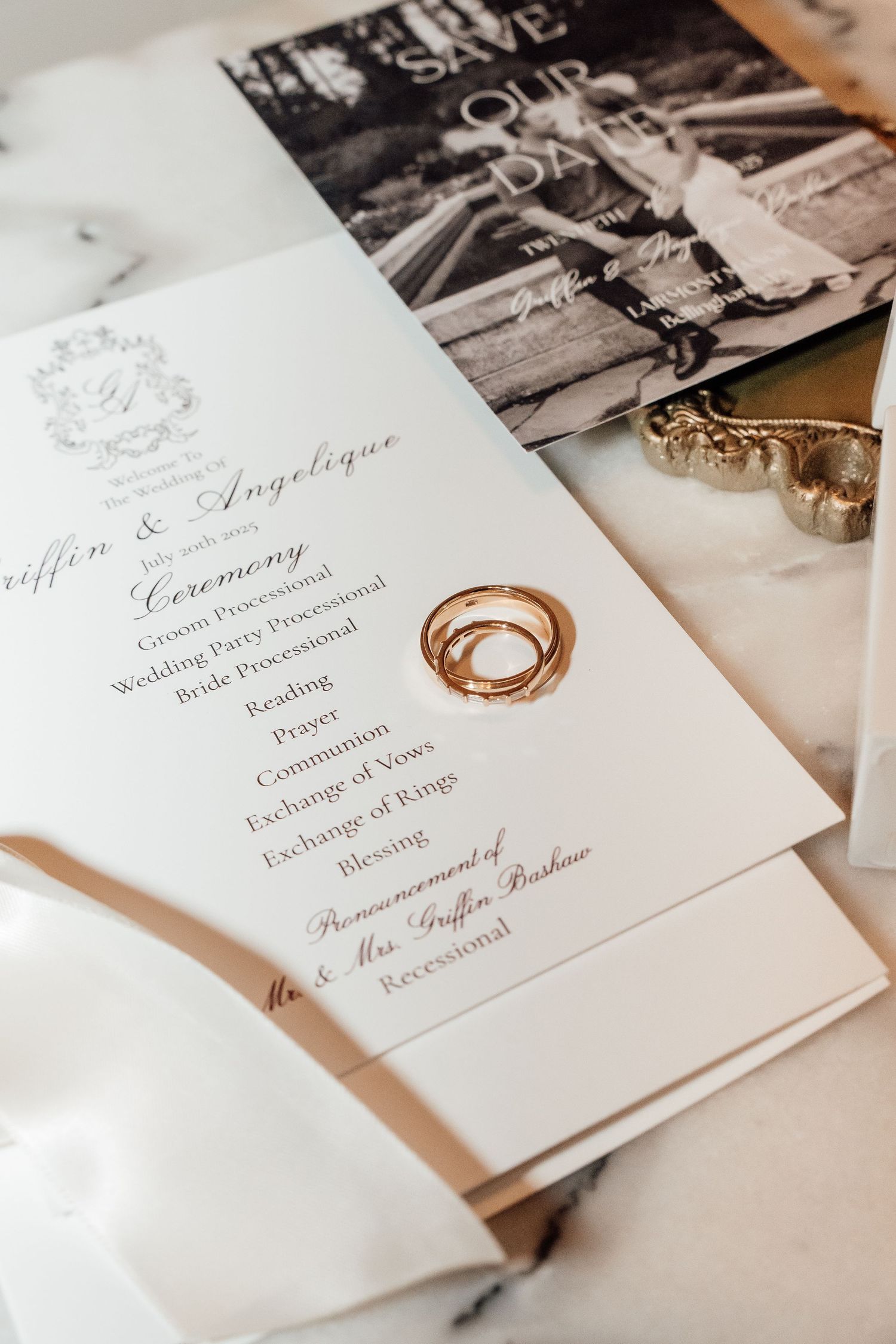 Elegant wedding ceremony program with gold rings displayed on white marble surface.