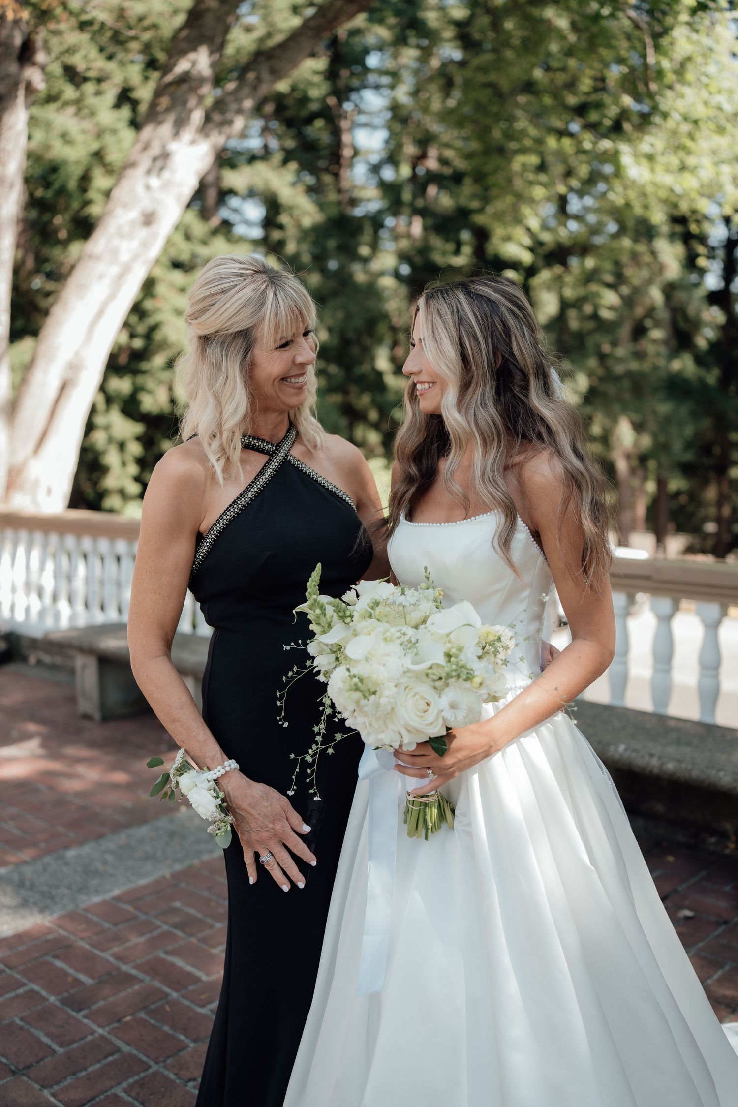 A touching moment between a bride in white and companion in black at an outdoor wedding venue.