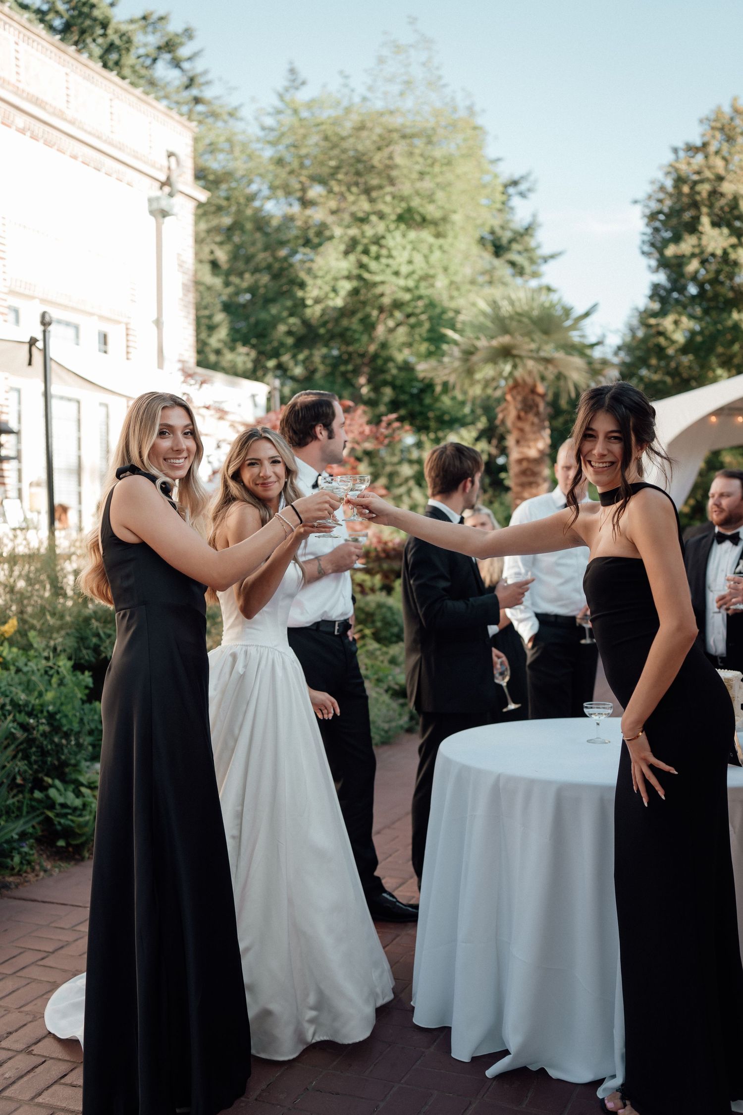 Guests gather on an outdoor patio during a wedding reception, dancing and celebrating around cocktail tables at dusk.