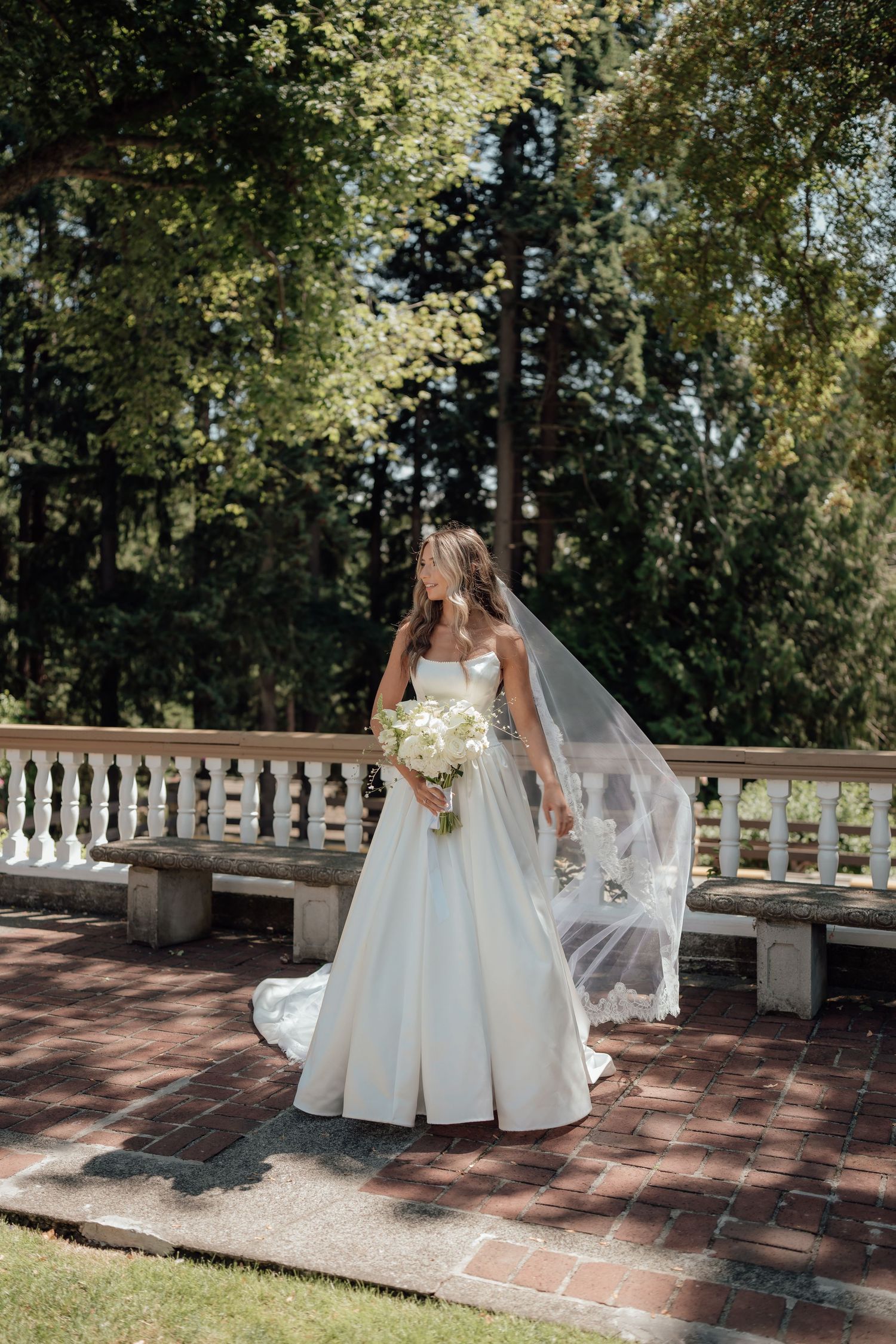 Classic white wedding dress with cathedral veil photographed on brick terrace surrounded by lush gardens.