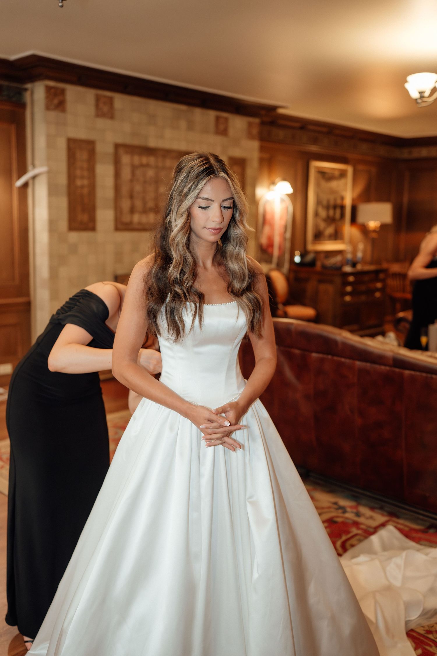 Flowing white ball gown wedding dress with pleated details shown in an elegant indoor setting.