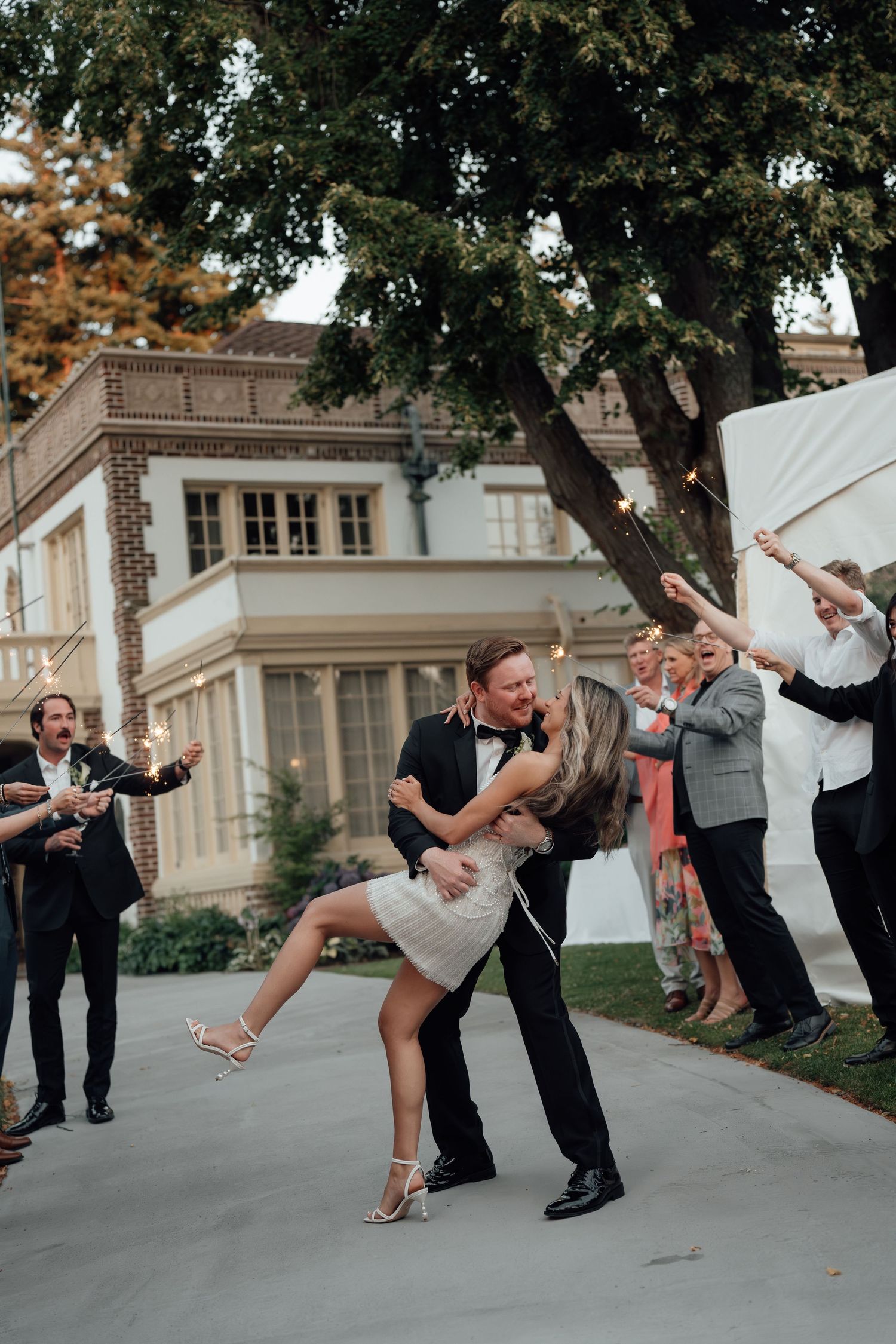 A romantic dip during a wedding celebration with guests cheering outside a mansion.