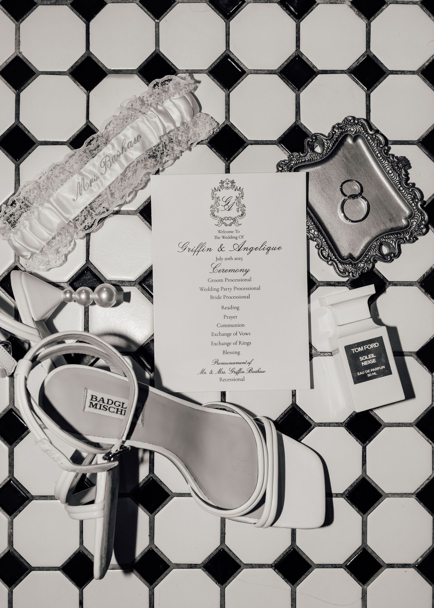 Wedding details including invitation, shoes, and decorative items arranged on a black and white tiled floor.