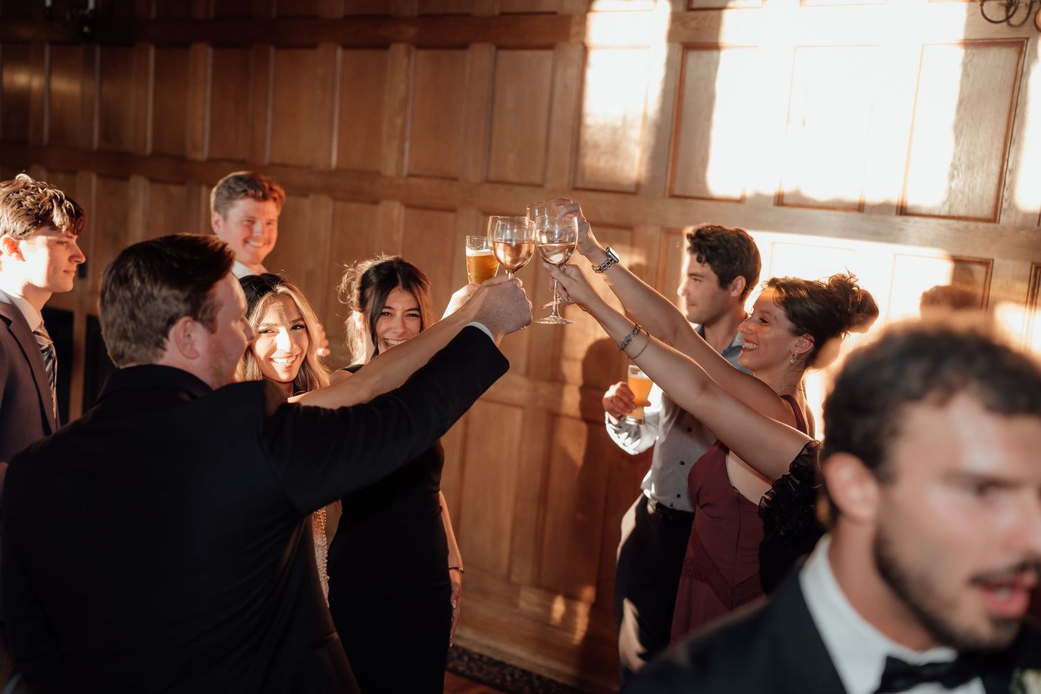 Wedding party toasting with champagne glasses in a warm-lit wooden reception hall.