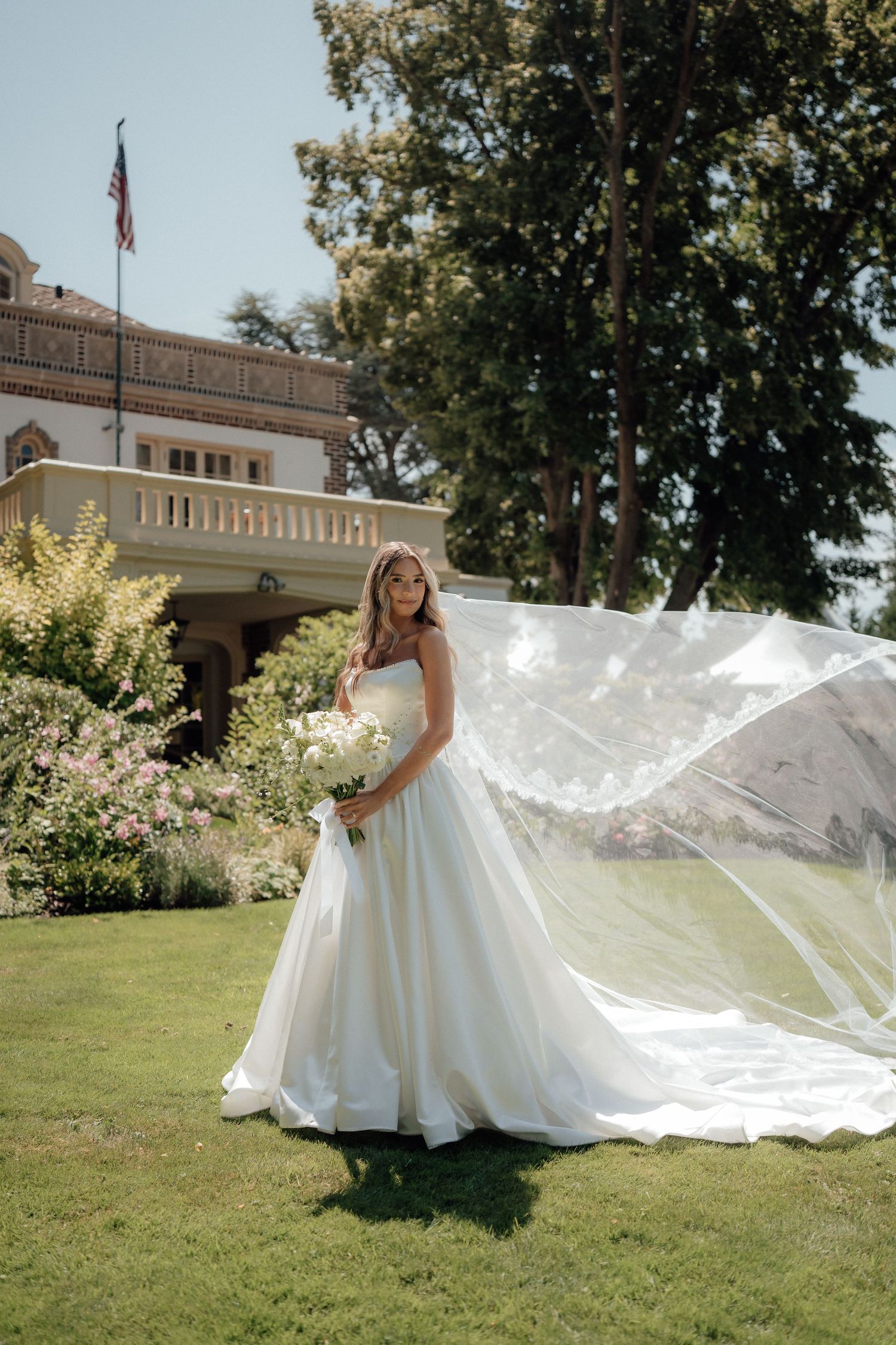 A stunning bridal portrait outdoors with a flowing veil catching the wind on a sunny day at an elegant venue.