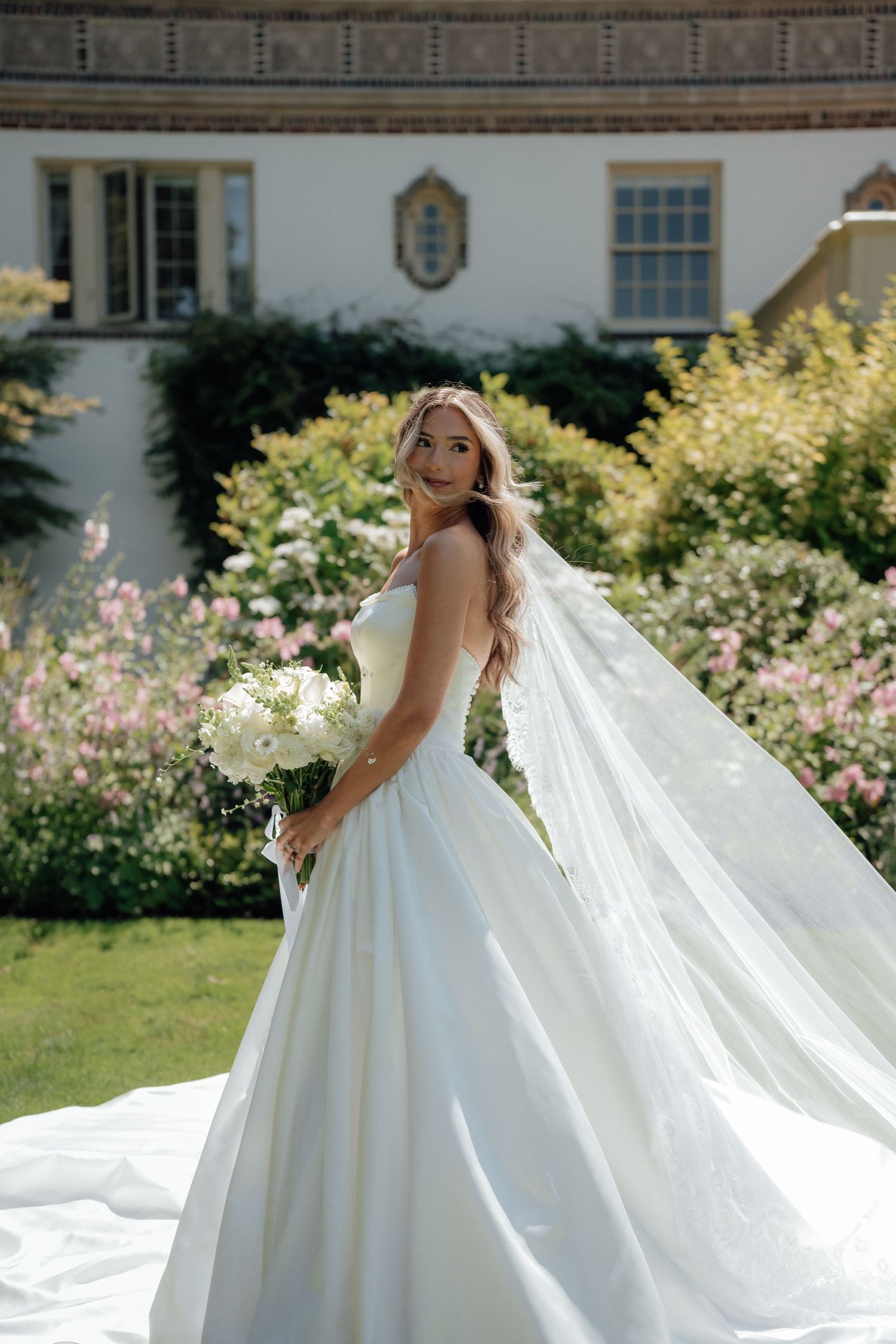 A stunning bridal portrait showcasing a flowing white dress and cathedral veil against a garden backdrop.