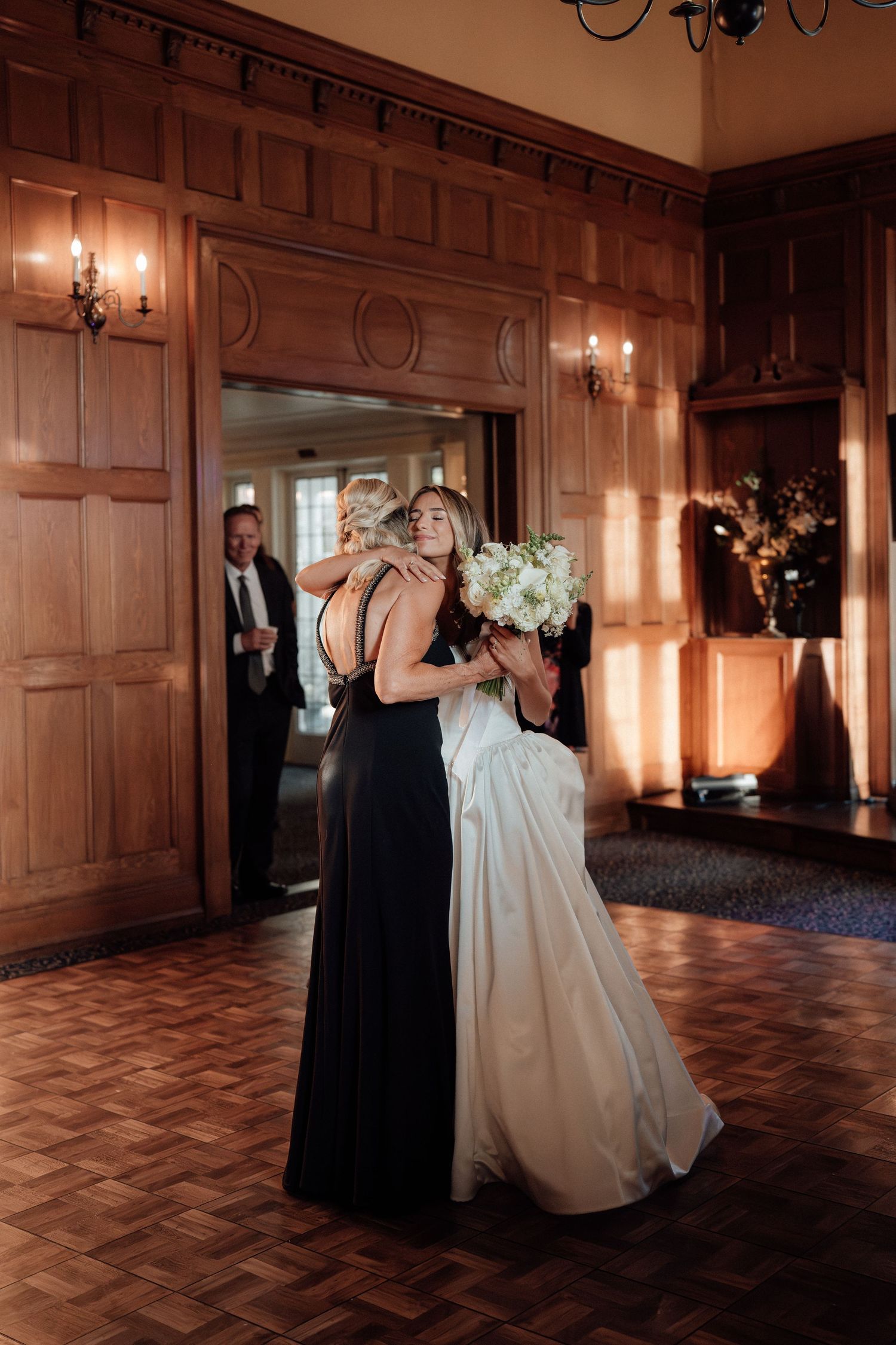 An emotional embrace during a wedding reception in an elegant wood-paneled ballroom.