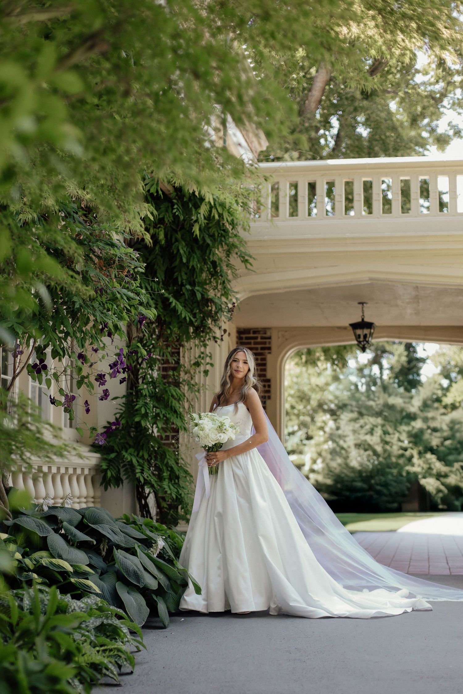 Elegant bridal portrait under a white architectural archway surrounded by lush garden foliage.