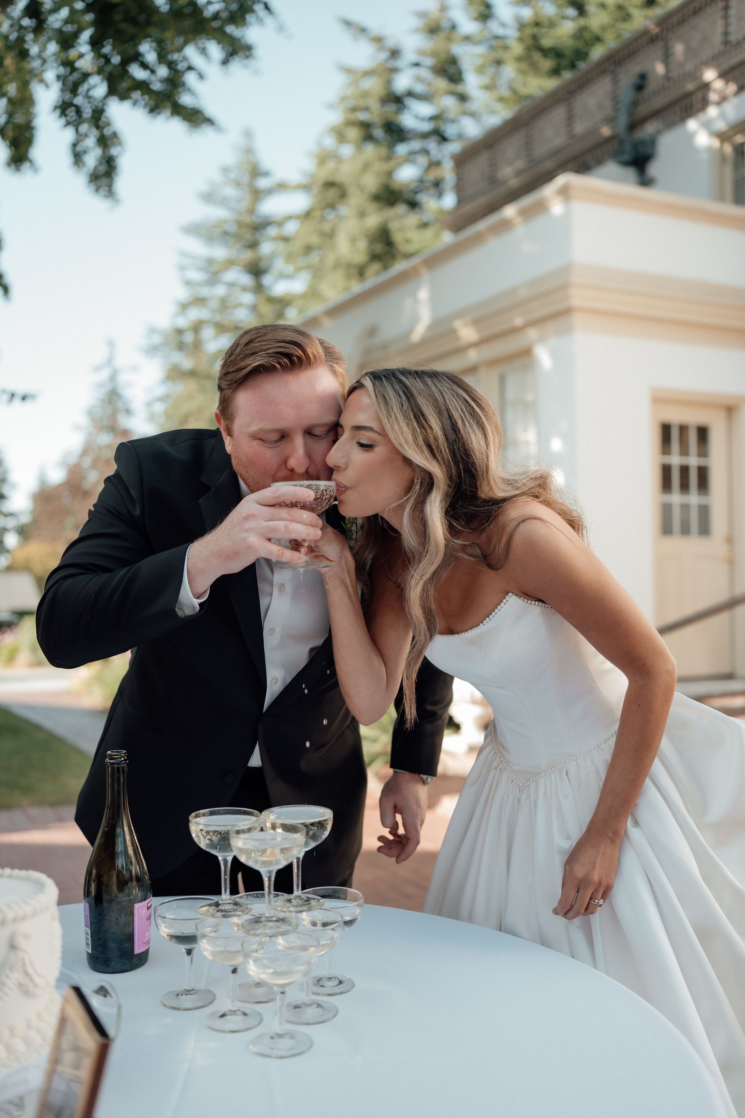 A couple sharing champagne at an outdoor wedding reception table.