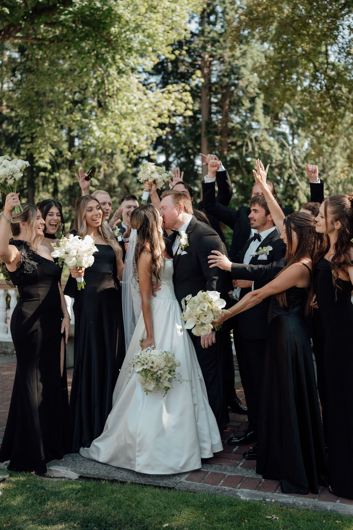 Wedding party in black dresses celebrates with the newlyweds outdoors.